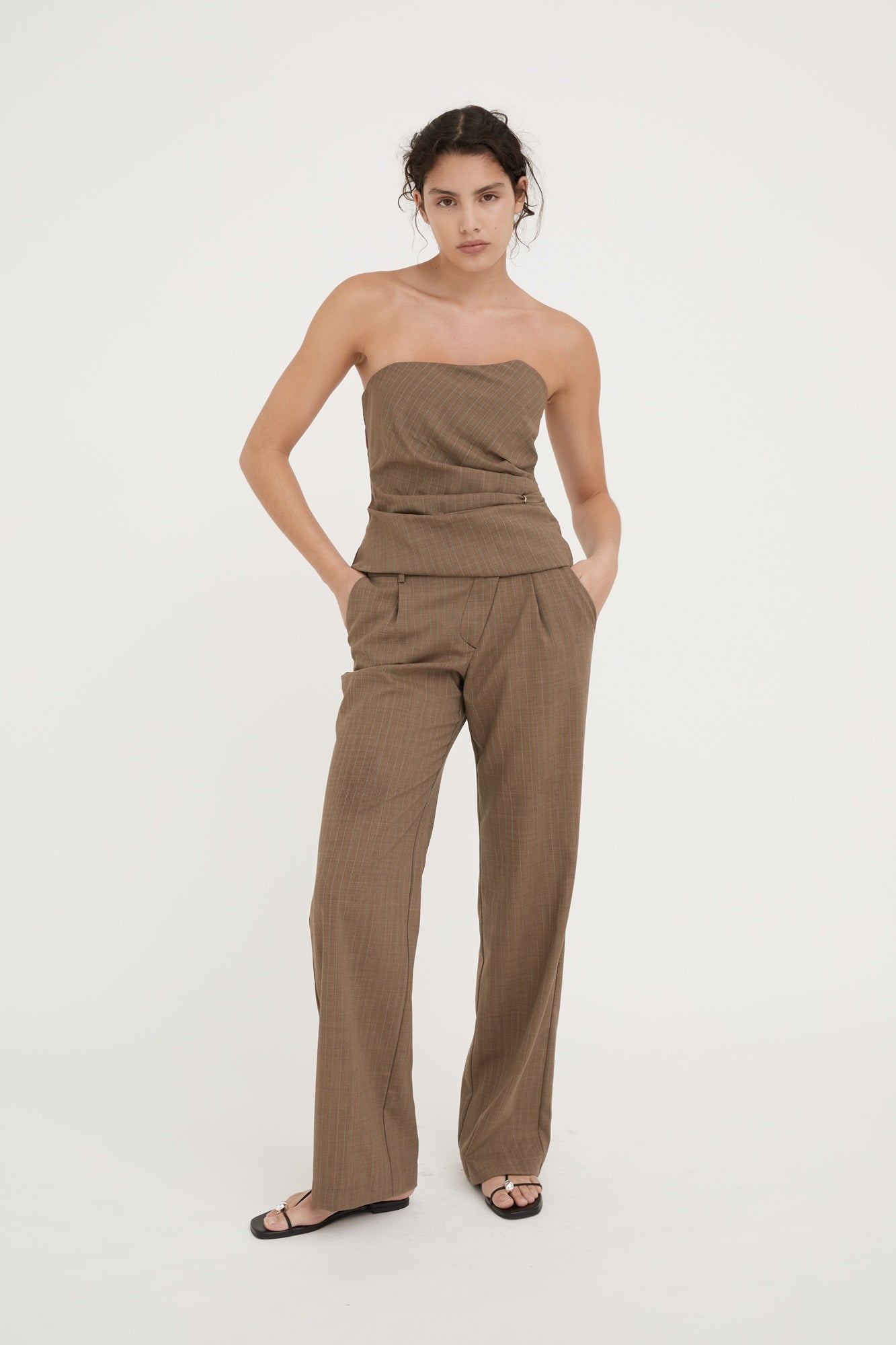 Woman wearing a brown strapless jumpsuit on a white background