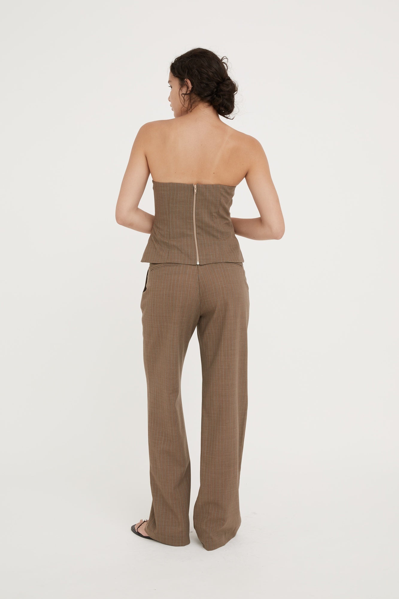Woman wearing a brown strapless top and wide-leg pants on a white background