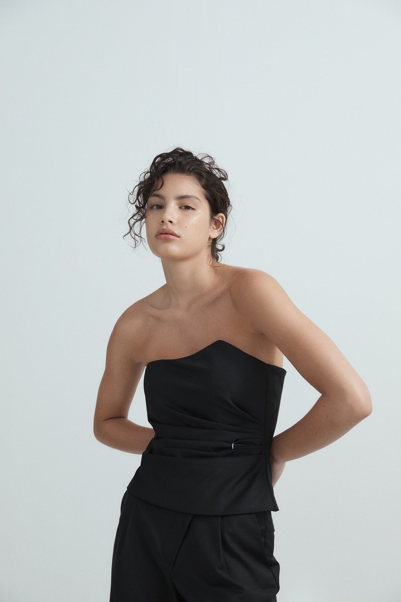 Woman wearing a black strapless top and black pants against a light gray background