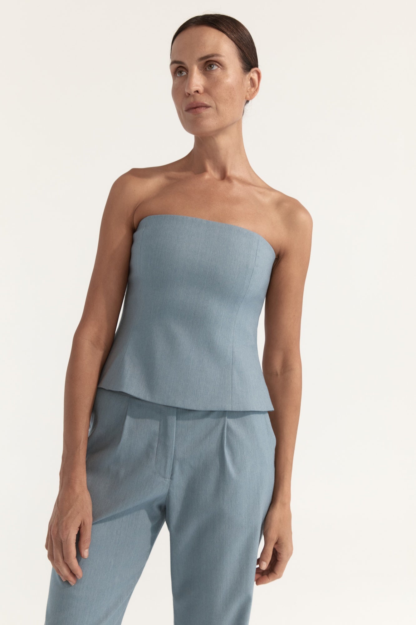 Woman wearing a light blue strapless top and pants on a plain background