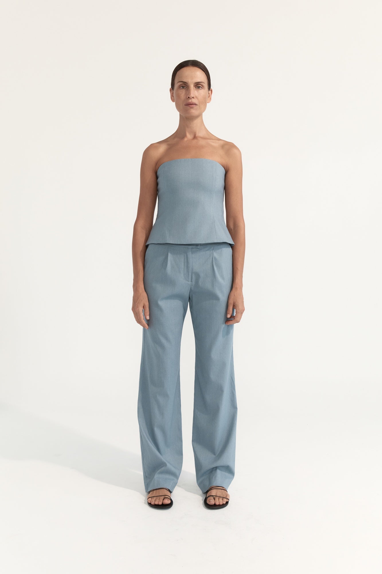 Woman wearing a light blue strapless top and pants on a white background