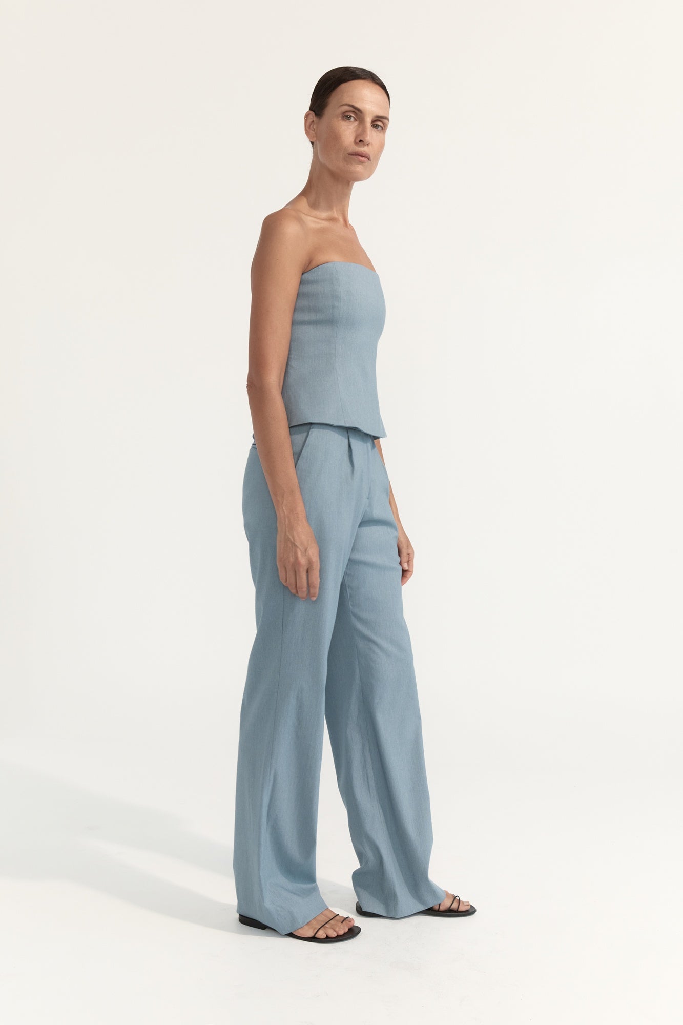 Woman wearing a light blue strapless top and wide-leg pants on a white background