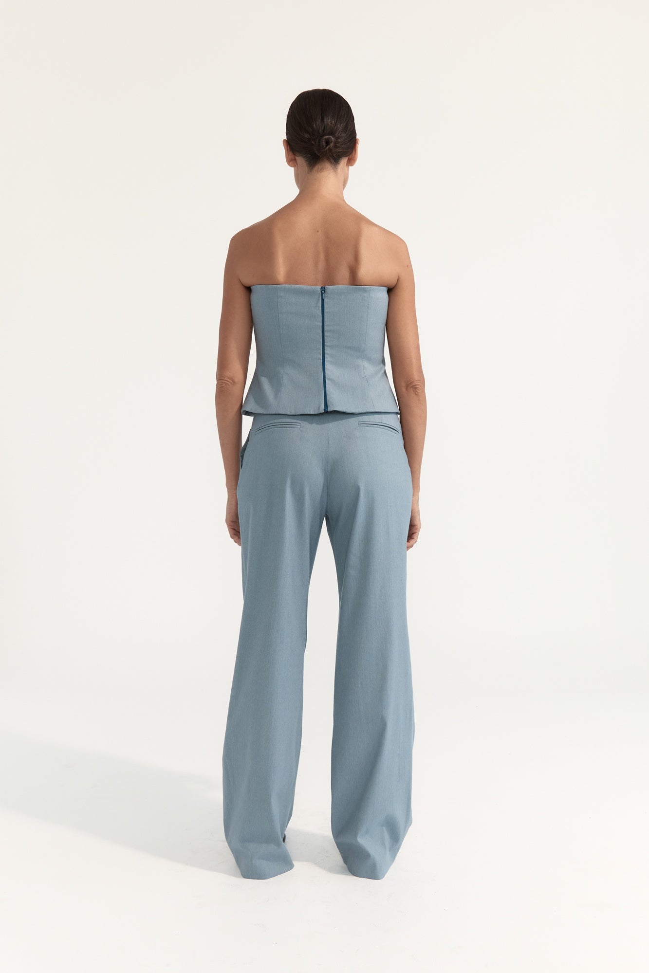Woman wearing a light blue strapless top and wide-leg pants on a white background