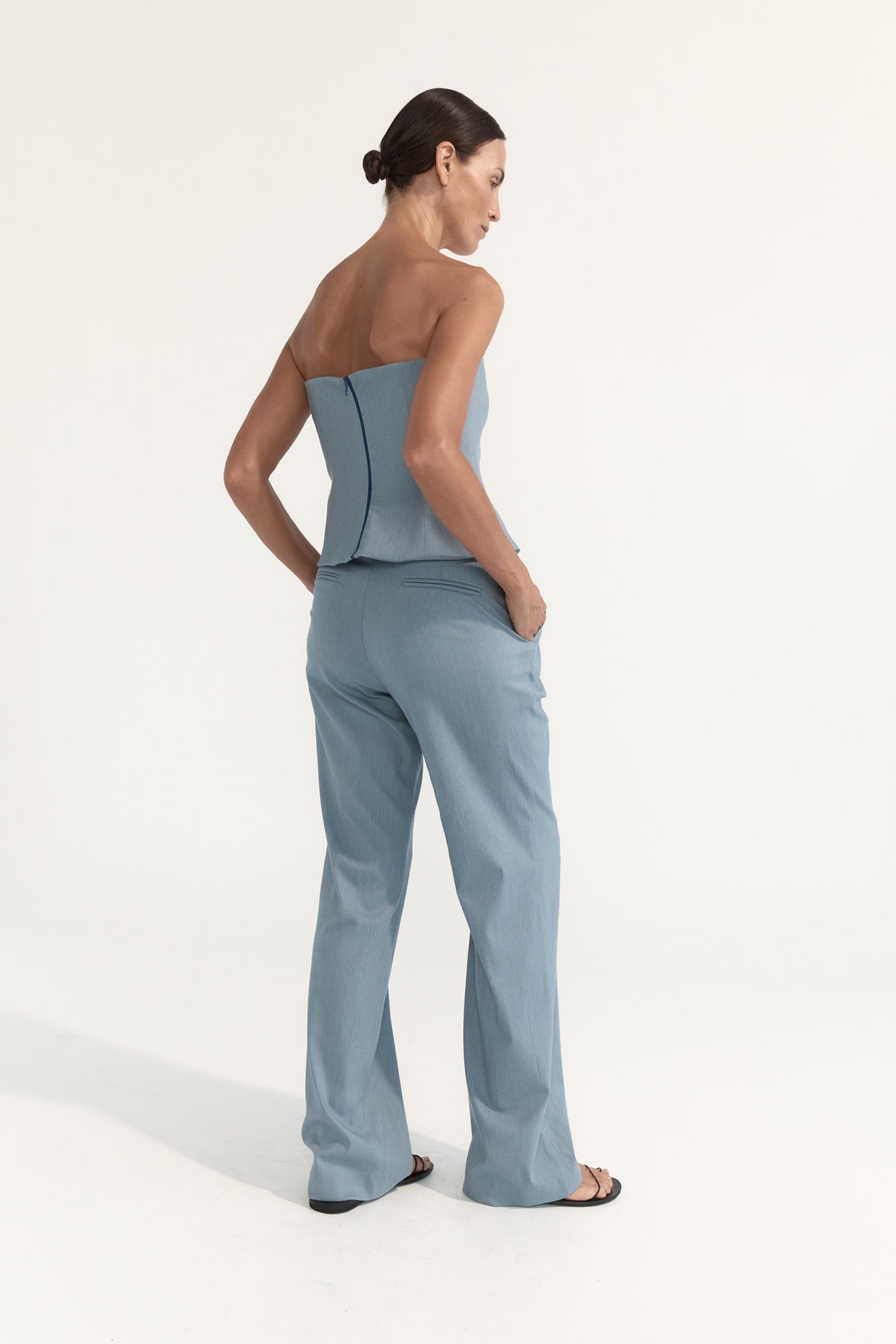 Woman wearing a light blue strapless top and pants on a white background