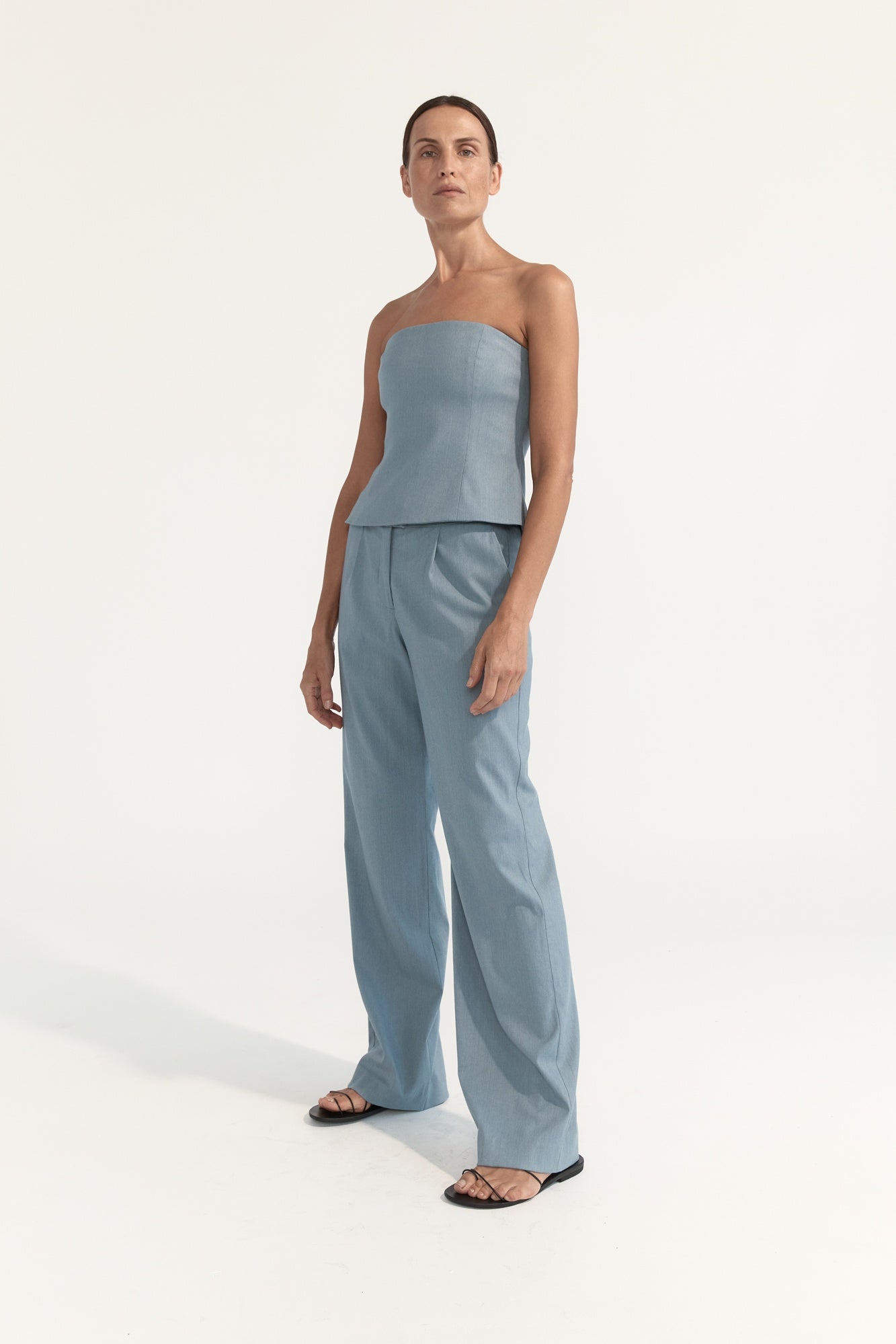 Woman wearing a light blue strapless top and wide-leg pants on a white background