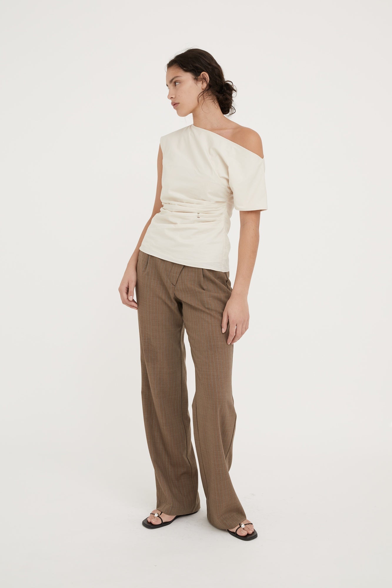 Woman wearing a white off-shoulder top and brown pants on a white background