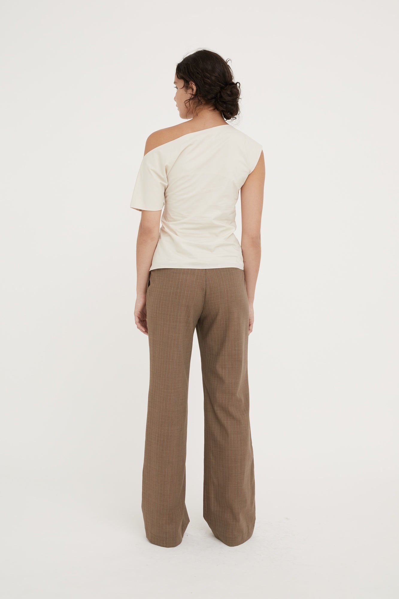 Woman wearing a white off-shoulder top and brown pants on a white background