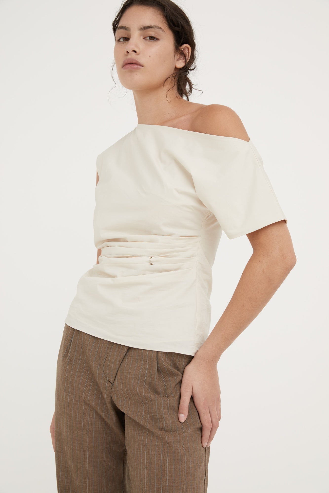 Woman wearing an off-shoulder cream top and brown pants on a white background