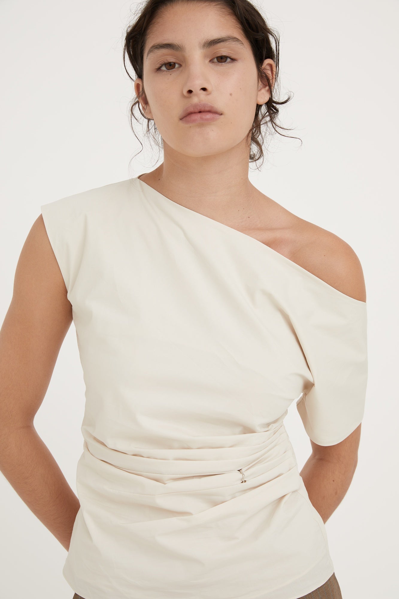 Woman wearing a white one-shoulder top against a plain background