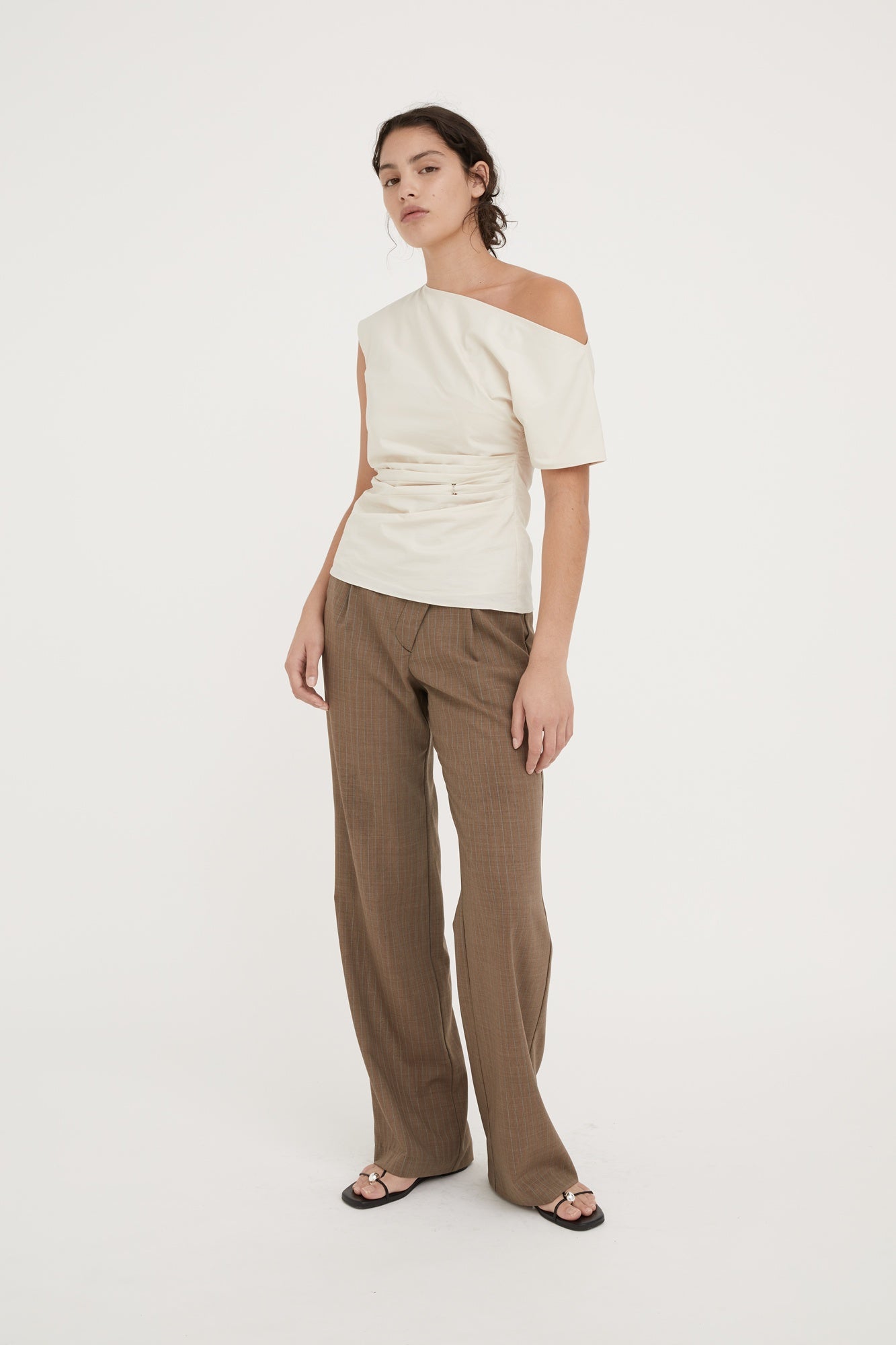 Woman wearing a white off-shoulder top and brown pants on a white background