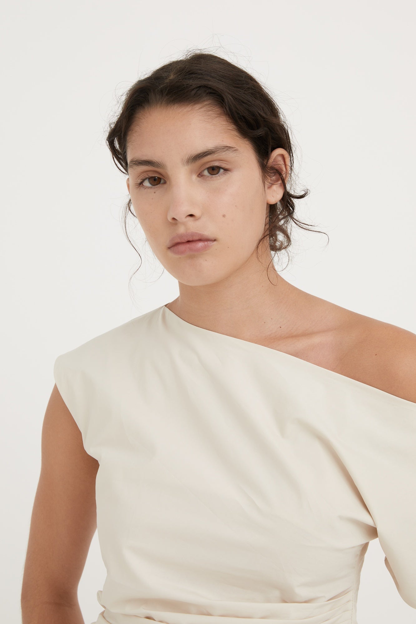 Woman wearing a one-shoulder beige top against a white background