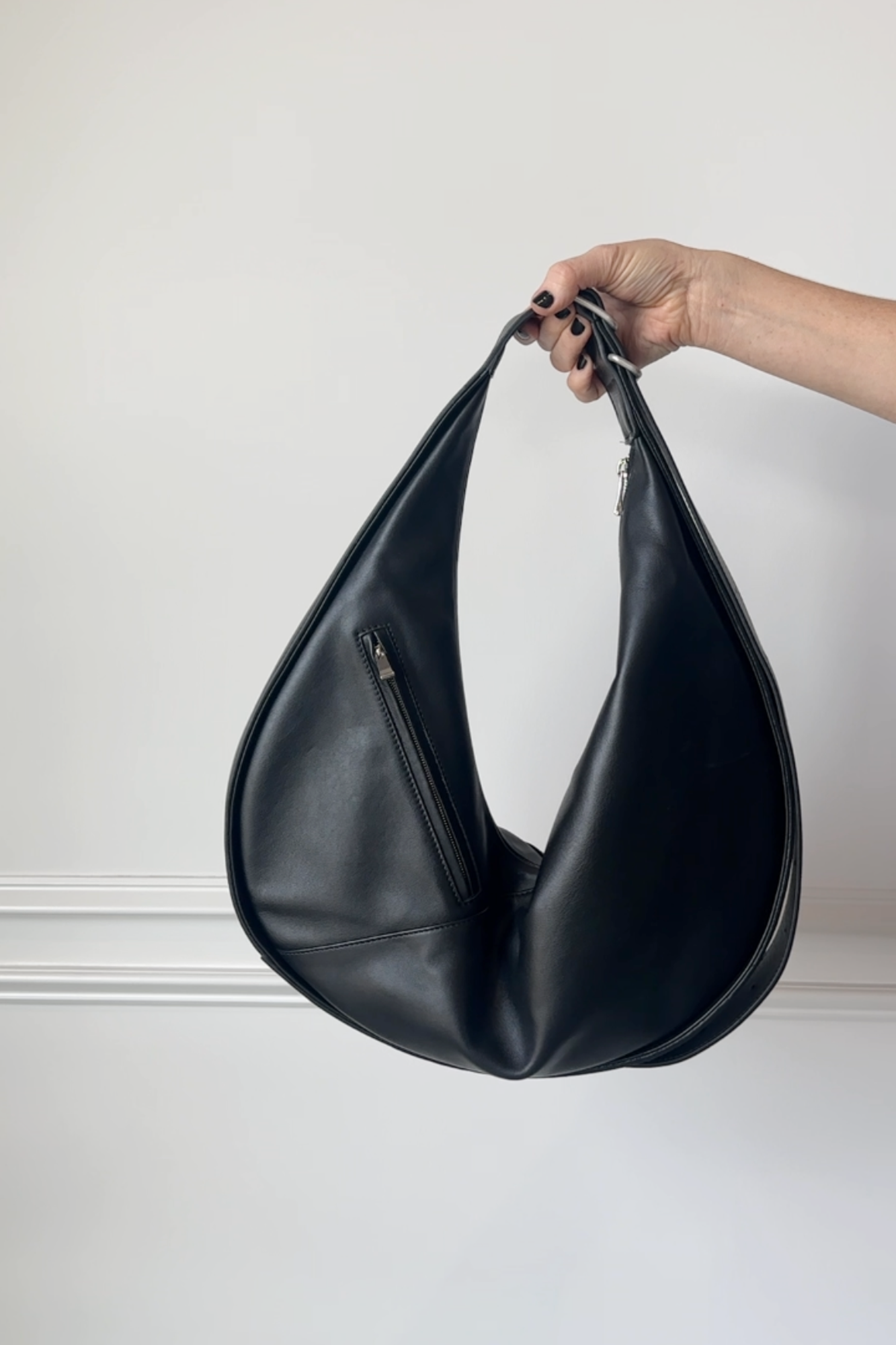 Black leather handbag held by a hand against a plain background