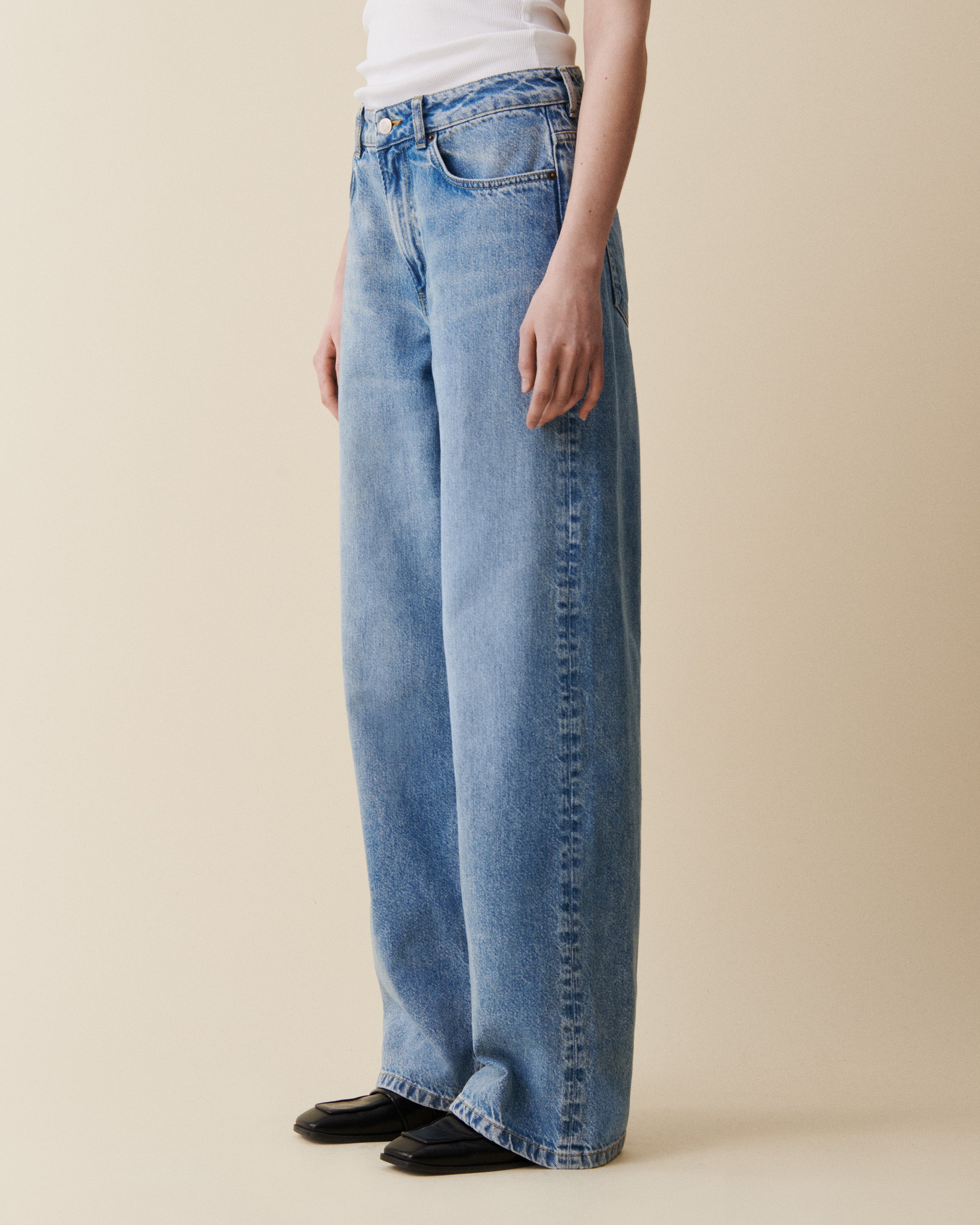 Person wearing light blue jeans on a beige background