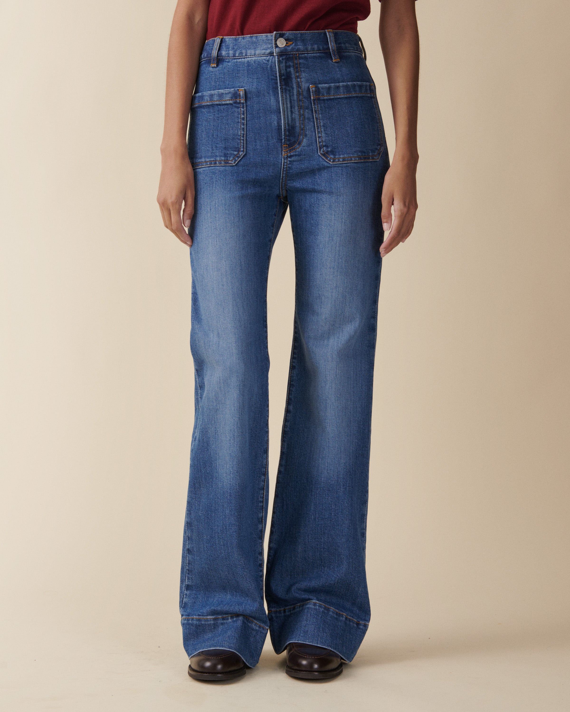 Person wearing blue flared jeans on a beige background