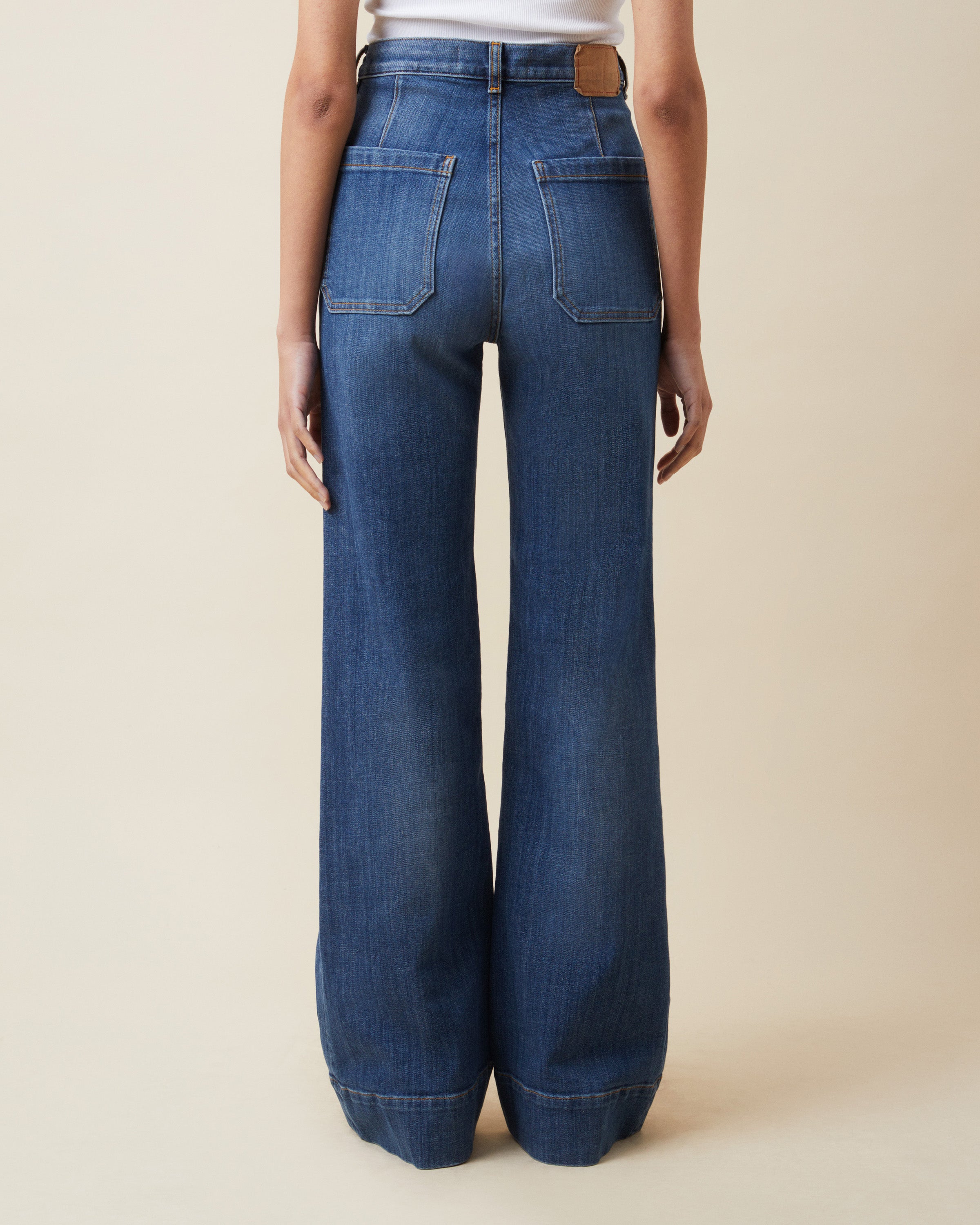 Person wearing blue wide-leg jeans on a beige background