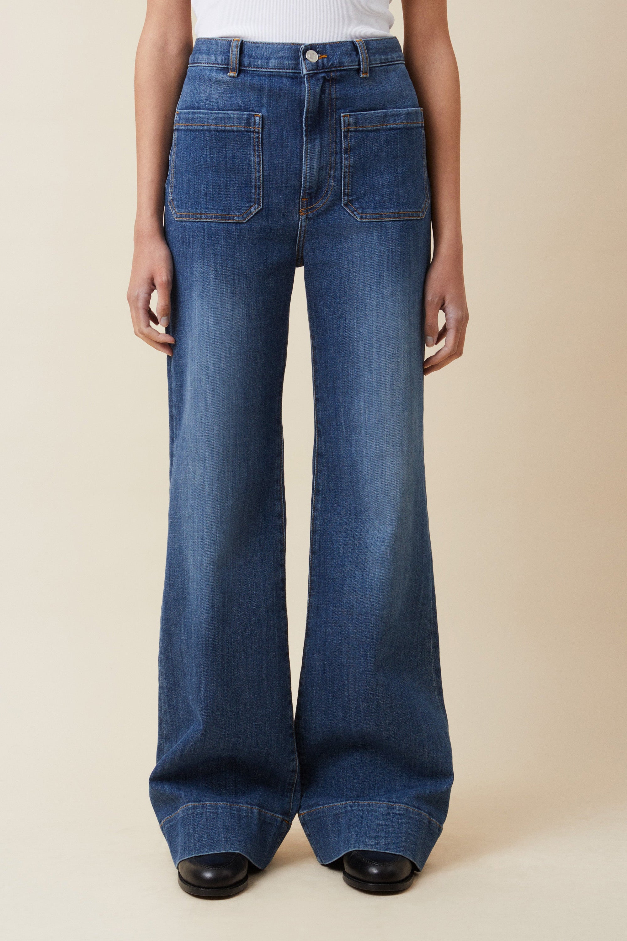 Person wearing blue flared jeans on a beige background