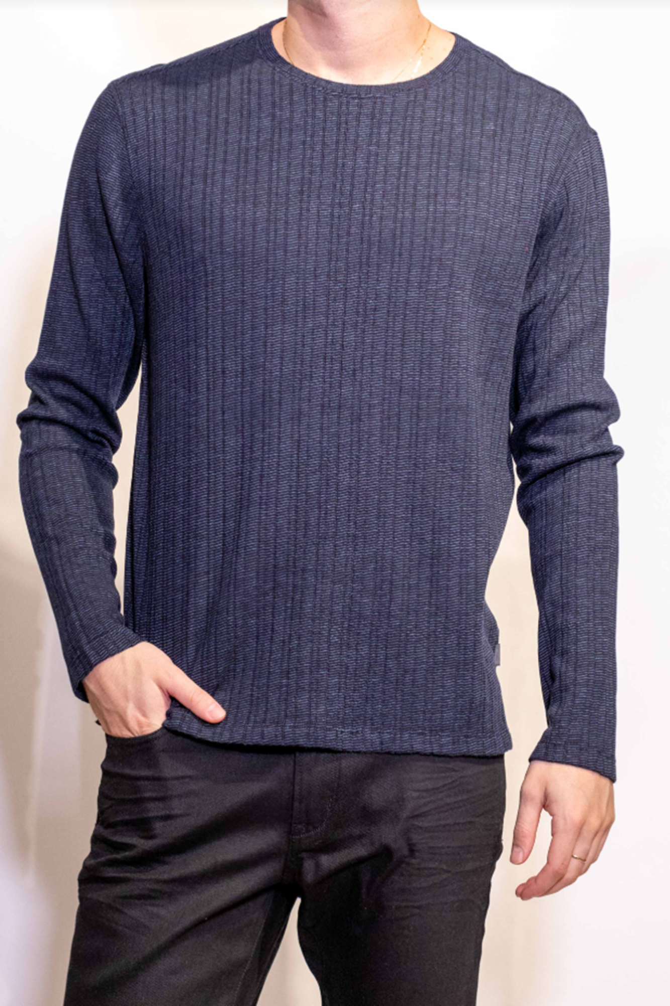 Person wearing a blue ribbed sweater and black pants against a plain background