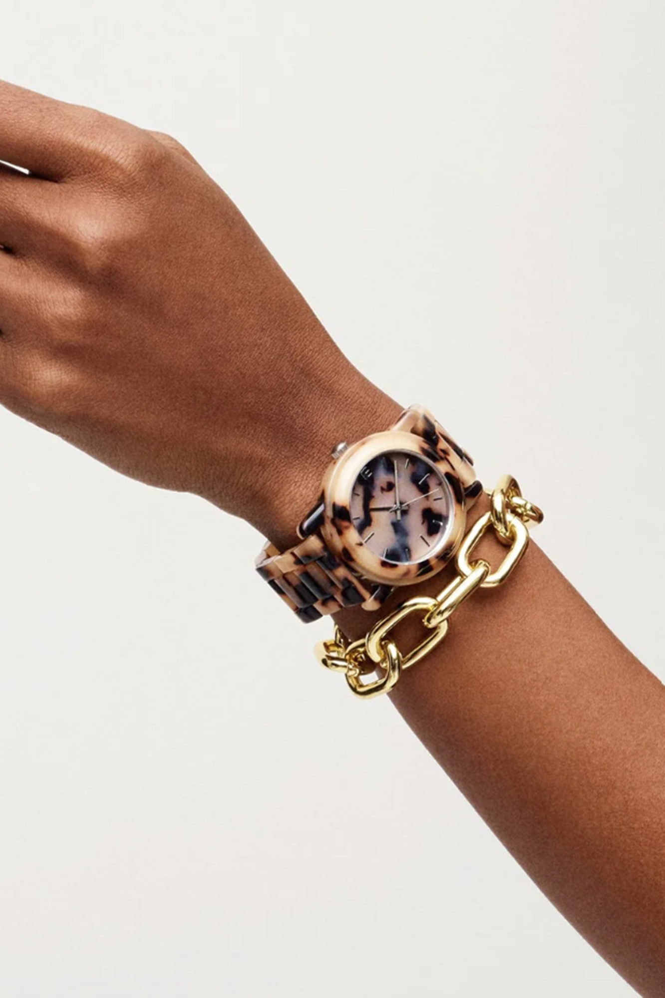 Leopard print watch on a wrist with a gold chain, against a plain background