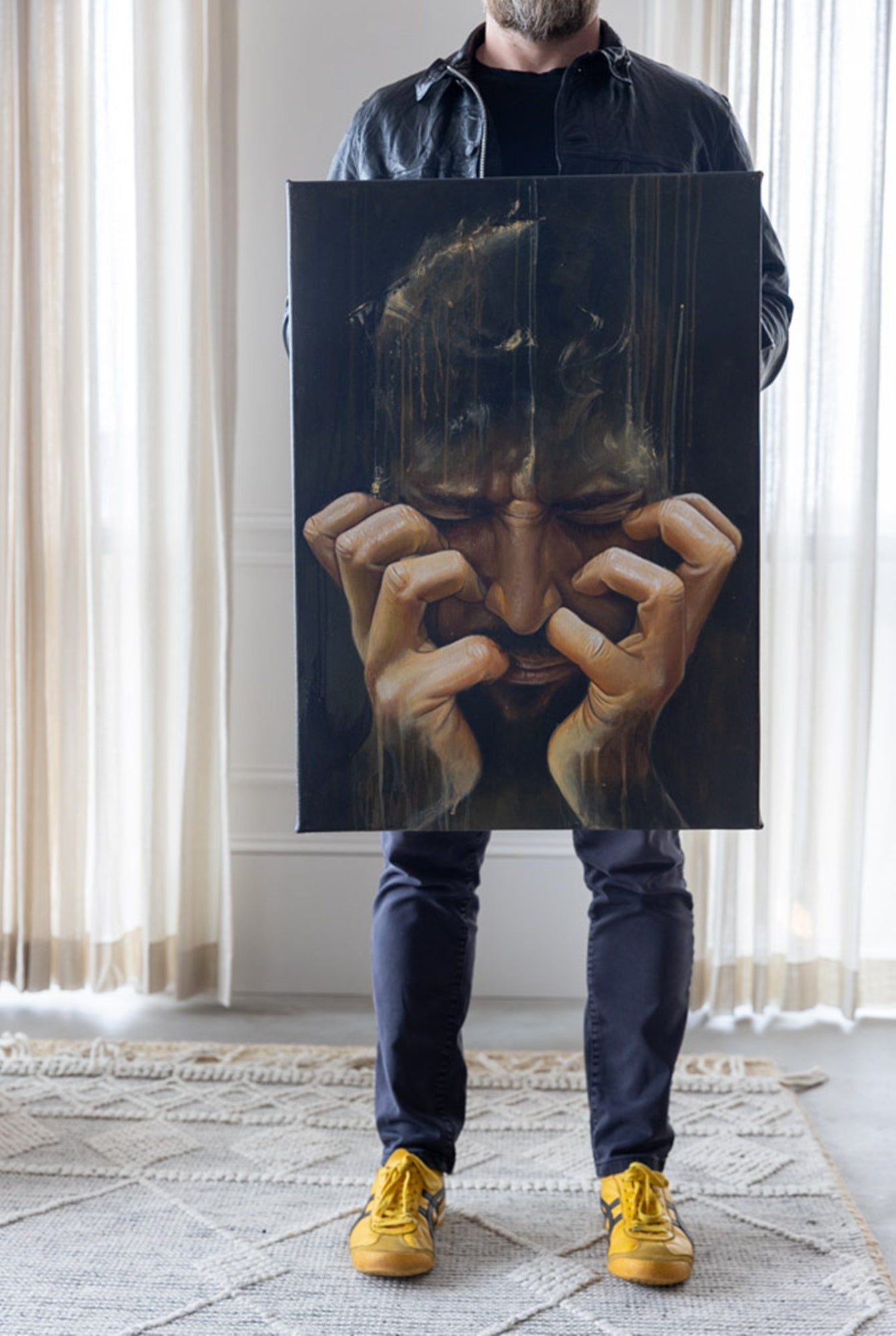 Person holding a large painting of a face with hands on a black background