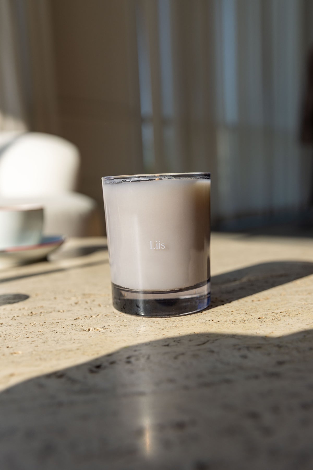 Liis hand-poured soy and coconut wax candle in a frosted glass vessel on a sunlit stone table