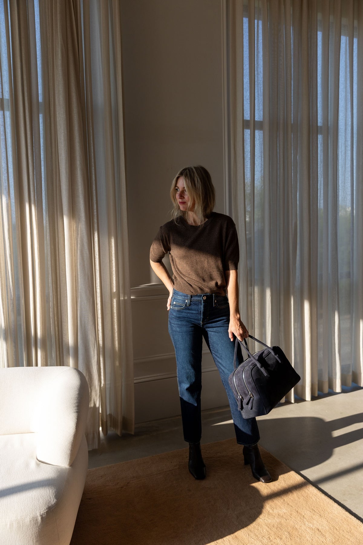 Lisa Yang Genevra T-Shirt in dark truffle with AMO jeans and A. Emery Talbot bag, full-length view in a sunlit room