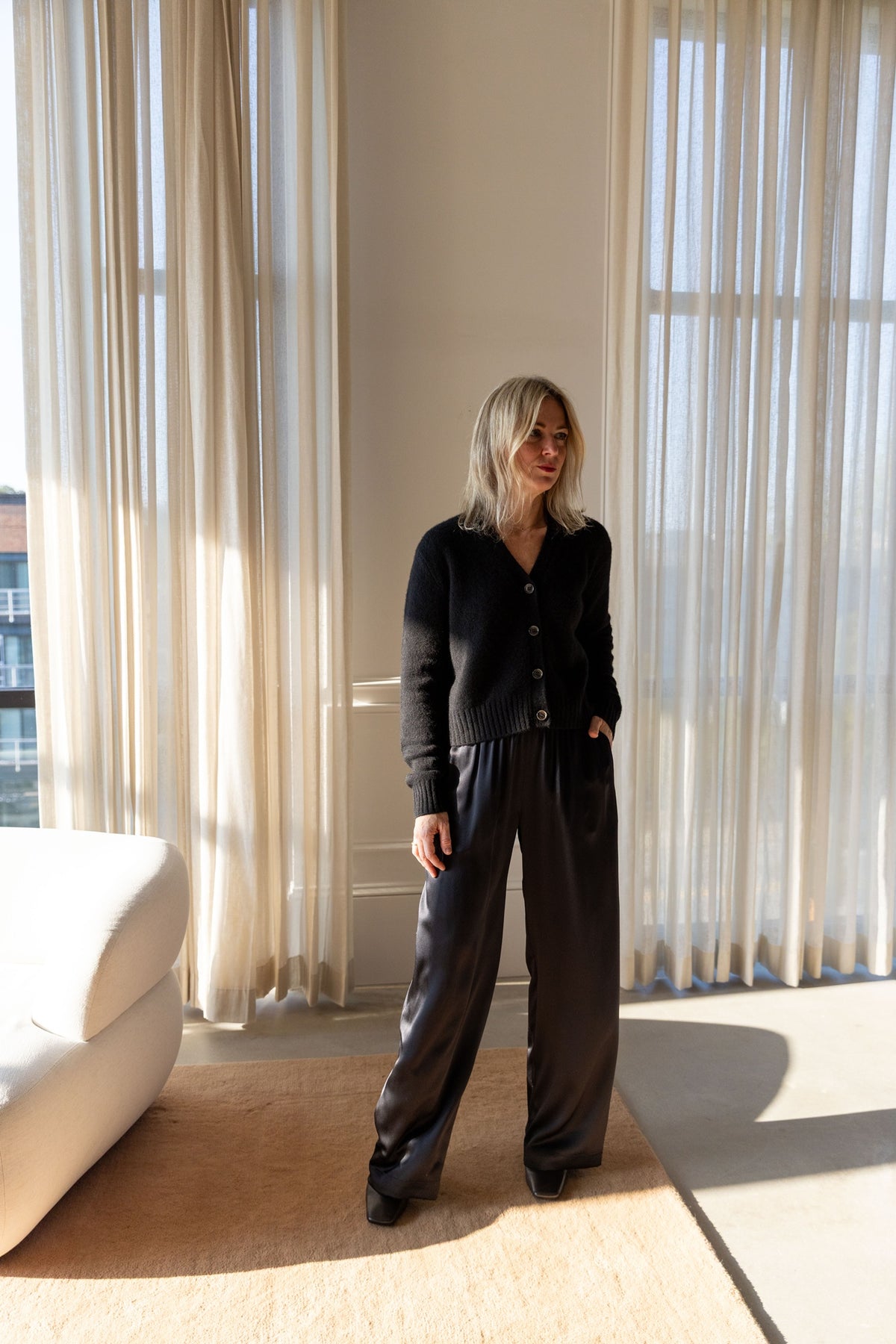 Lisa Yang Marionette Cardigan in black with wide-leg Sablyn Brynn silk pants, full-length view in a sunlit room