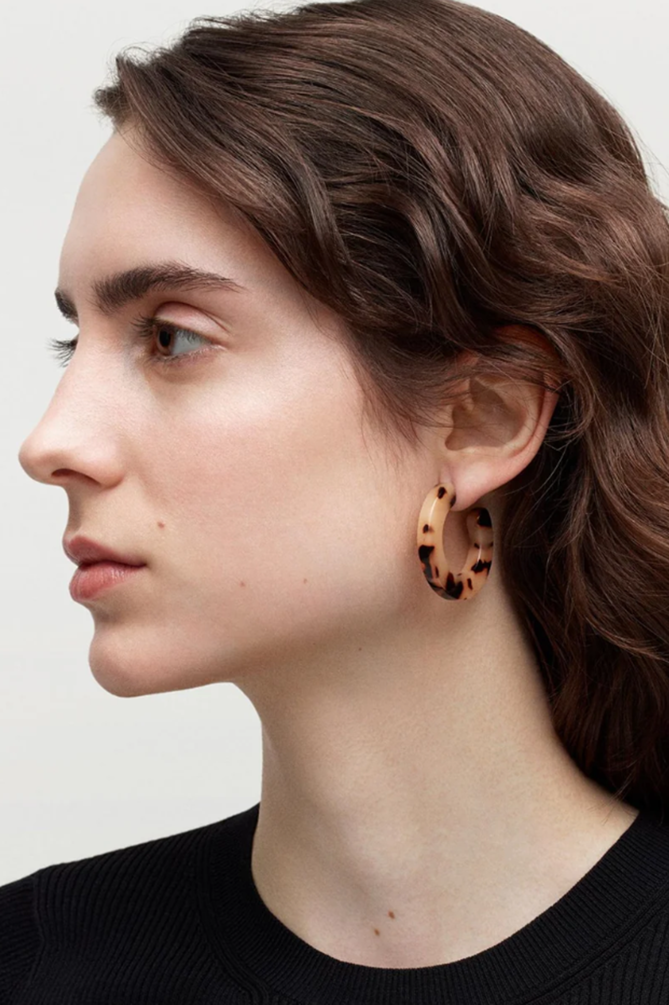 Woman wearing leopard print hoop earrings against a neutral background