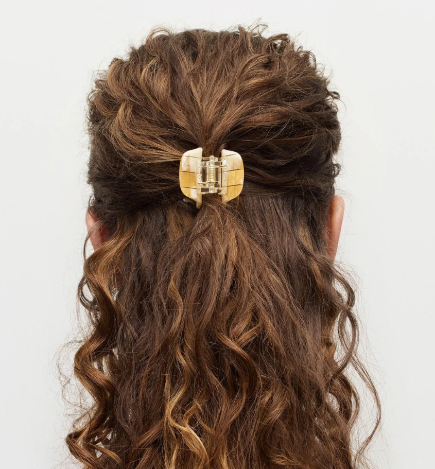 Gold hair clip in wavy brown hair on a white background