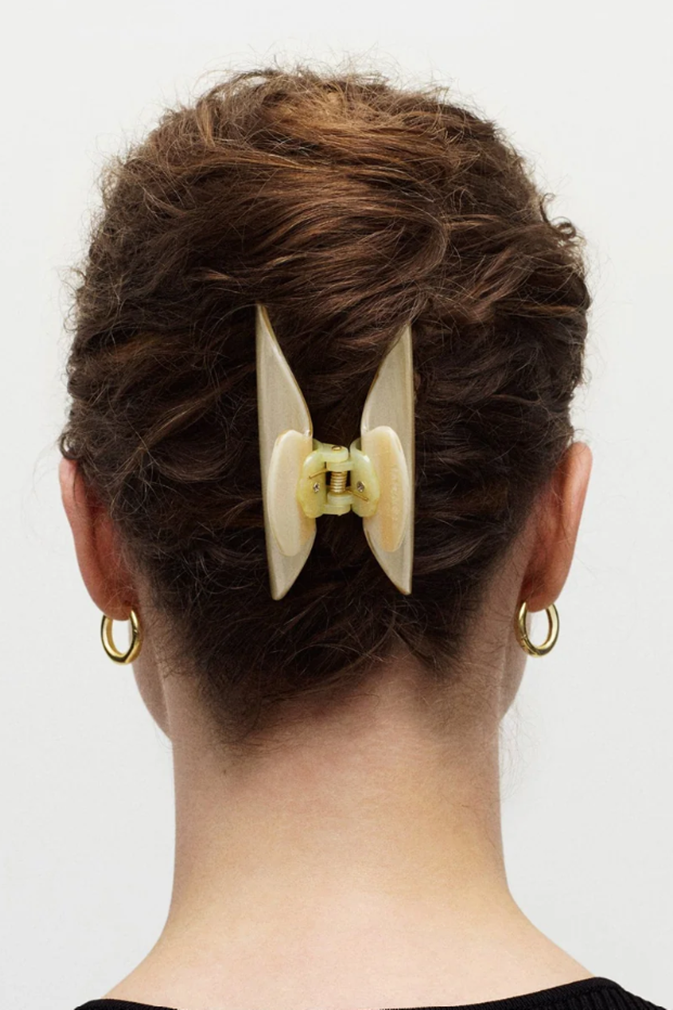 Back view of a person with a hair bun holding a decorative hair clip or claw against a white background