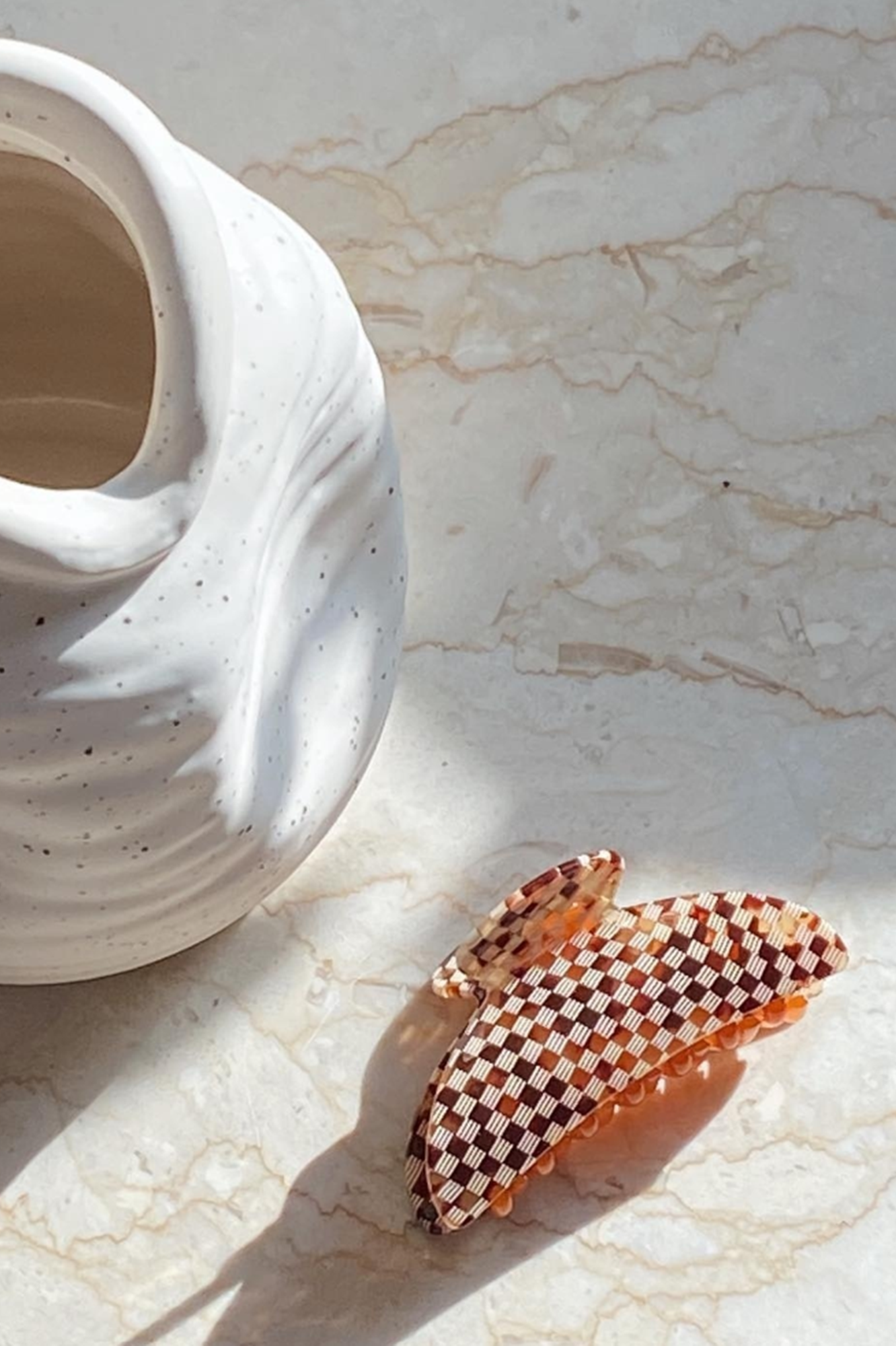 Checkered hair clip on a marble surface with a white ceramic vase