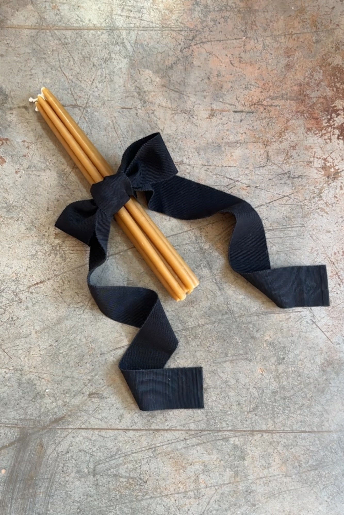 Two beeswax candles tied with a black ribbon on a textured surface