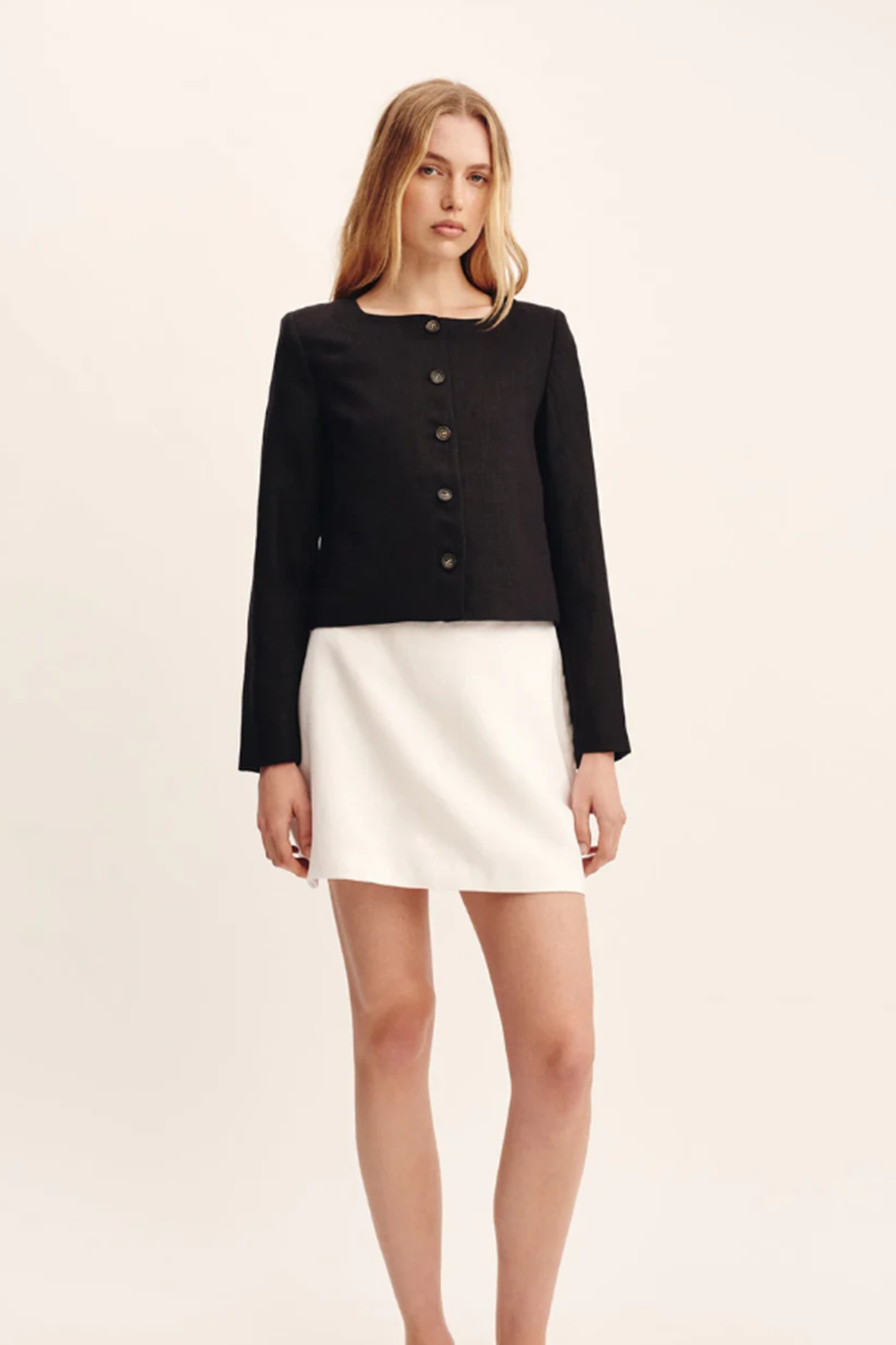Woman wearing a black jacket and white skirt on a beige background