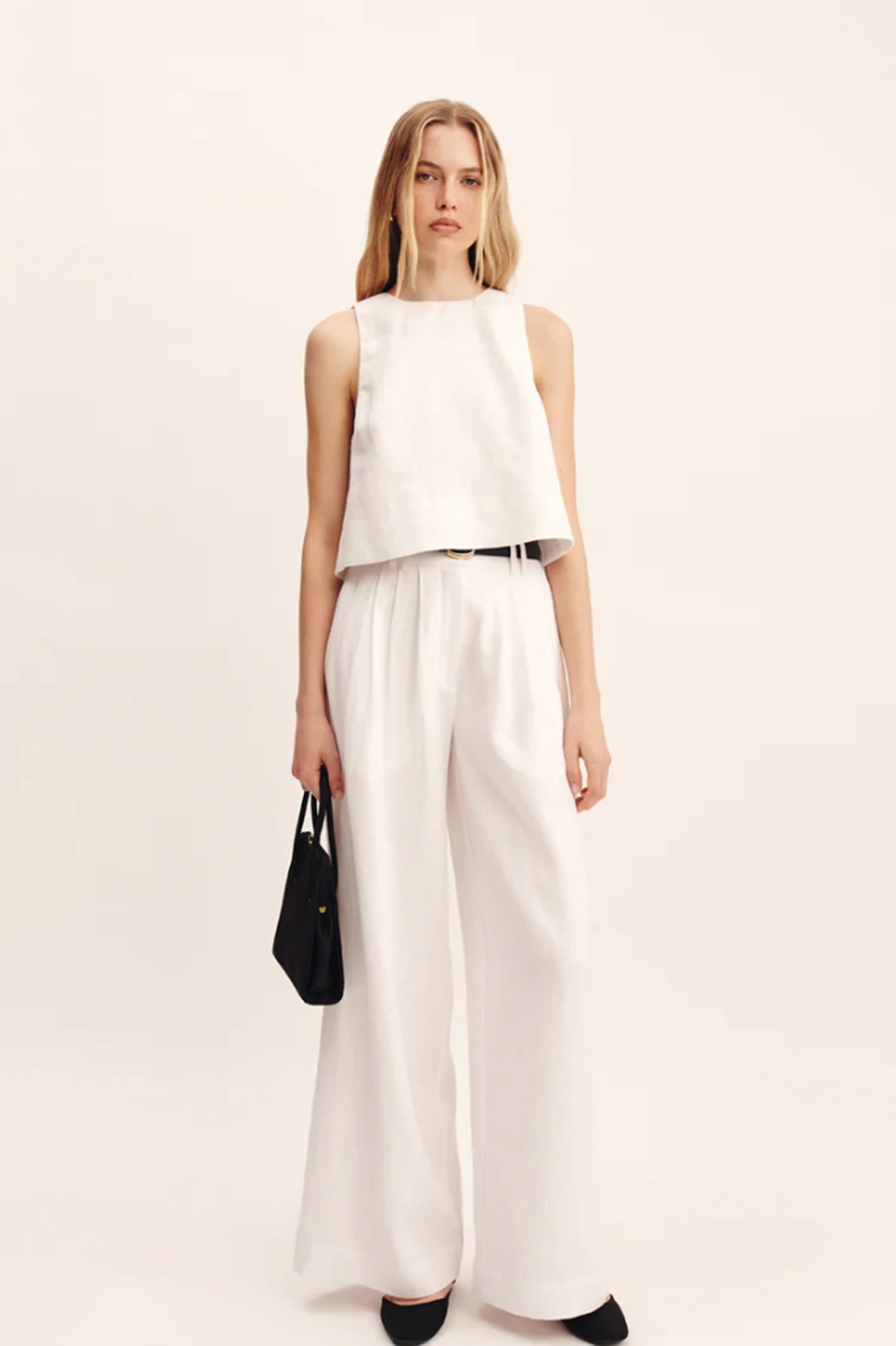Woman wearing a white sleeveless top and wide-leg pants on a beige background