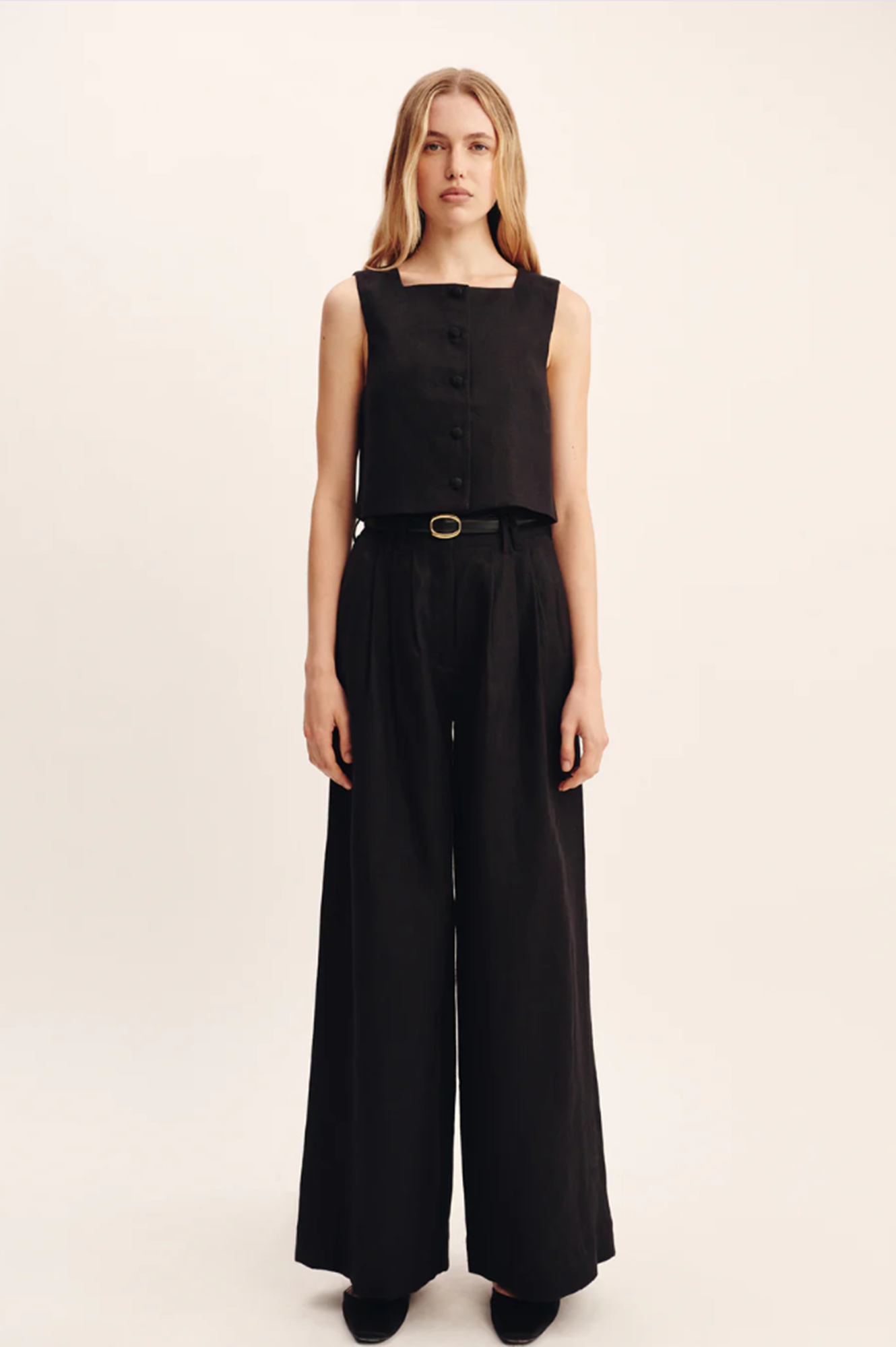 Woman wearing a black sleeveless top and wide-leg pants on a beige background