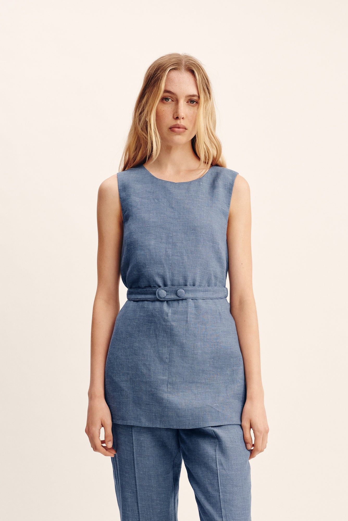 Woman wearing a blue sleeveless top and pants on a beige background