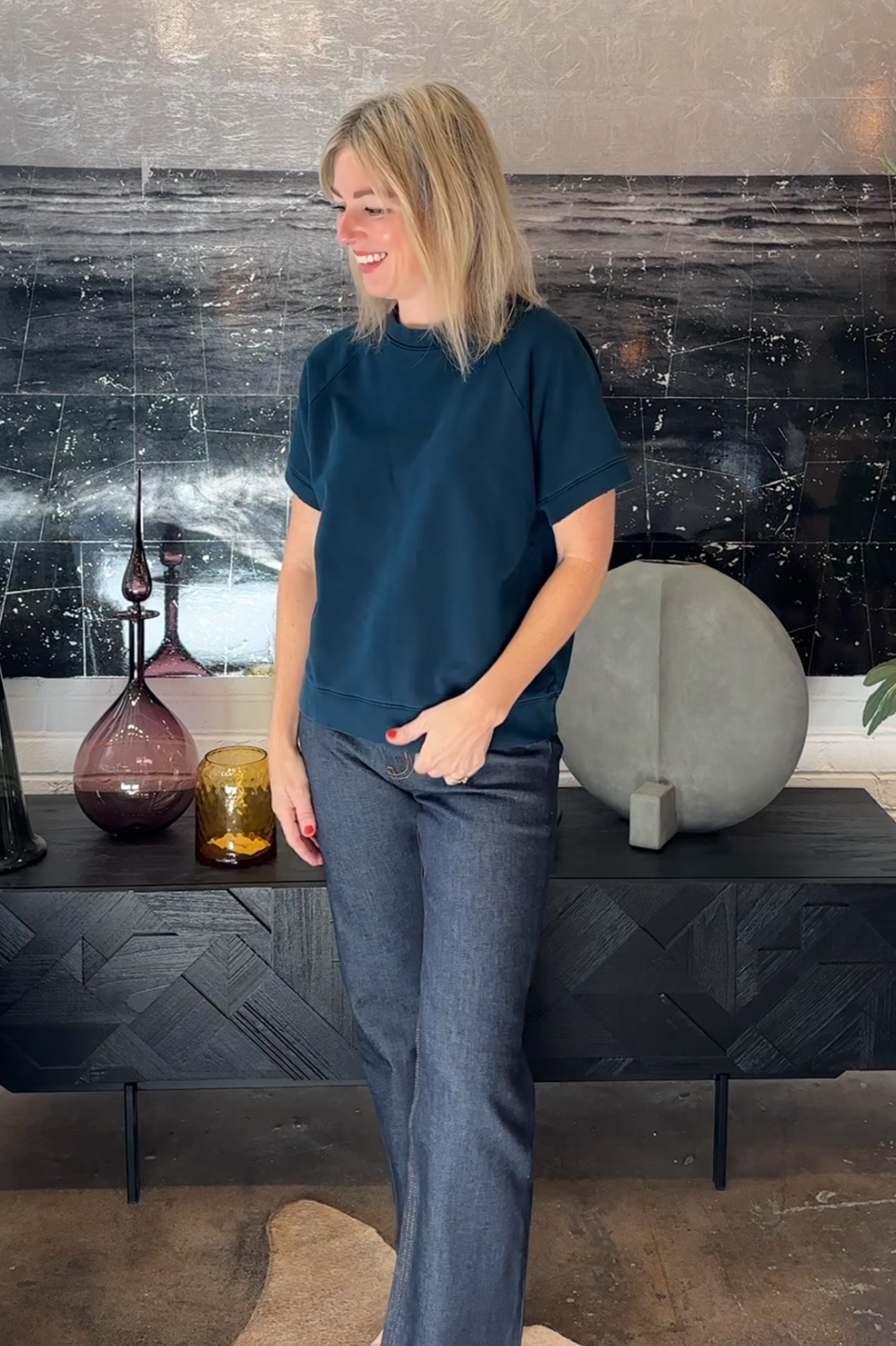 Woman in a blue shirt and jeans standing in front of a decorative wall with vases.