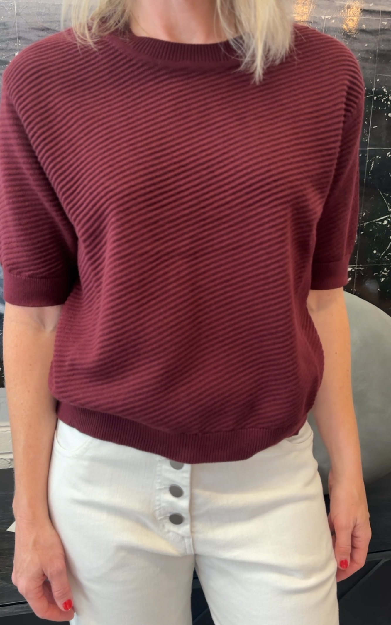 Person wearing a maroon ribbed sweater and white pants indoors.