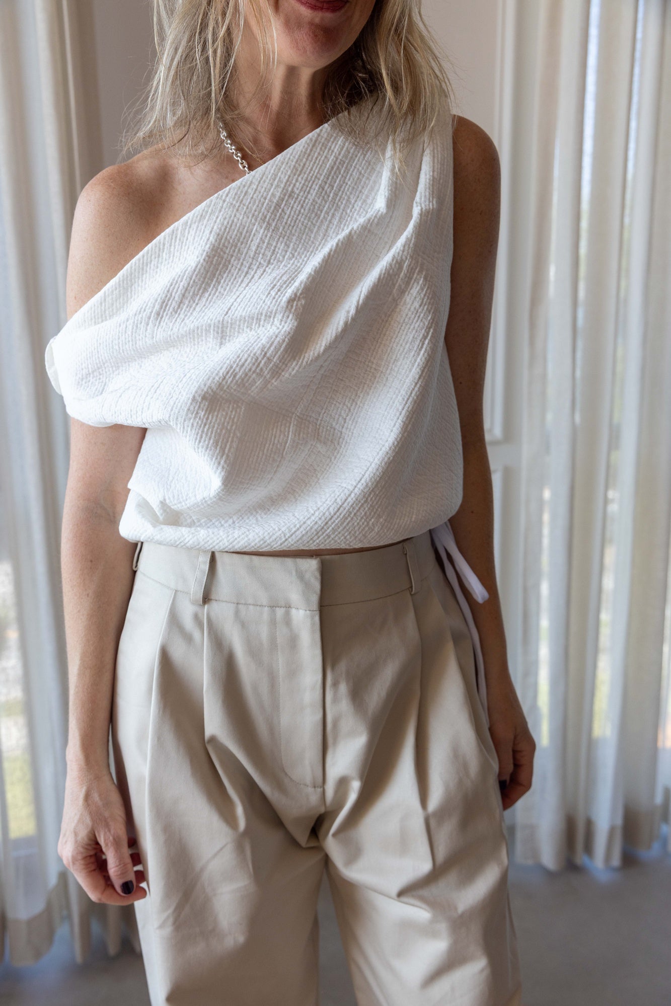Woman wearing the Rachel Comey Farfalla Top in white and the alfie tailored pant standing in front of white curtains