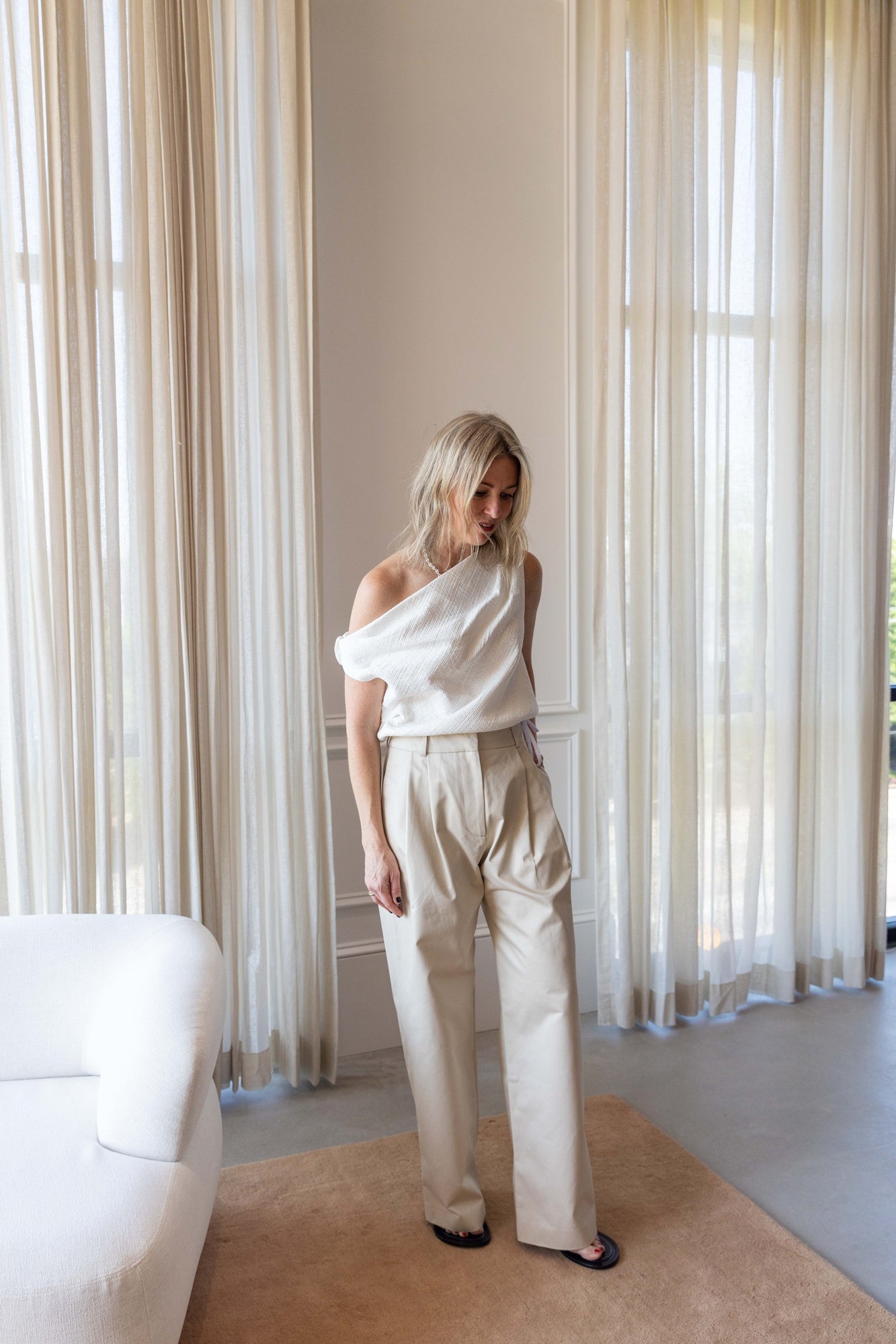 Woman wearing the Rachel Comey Farfalla Top in white and the alfie tailored pant standing in front of white curtains