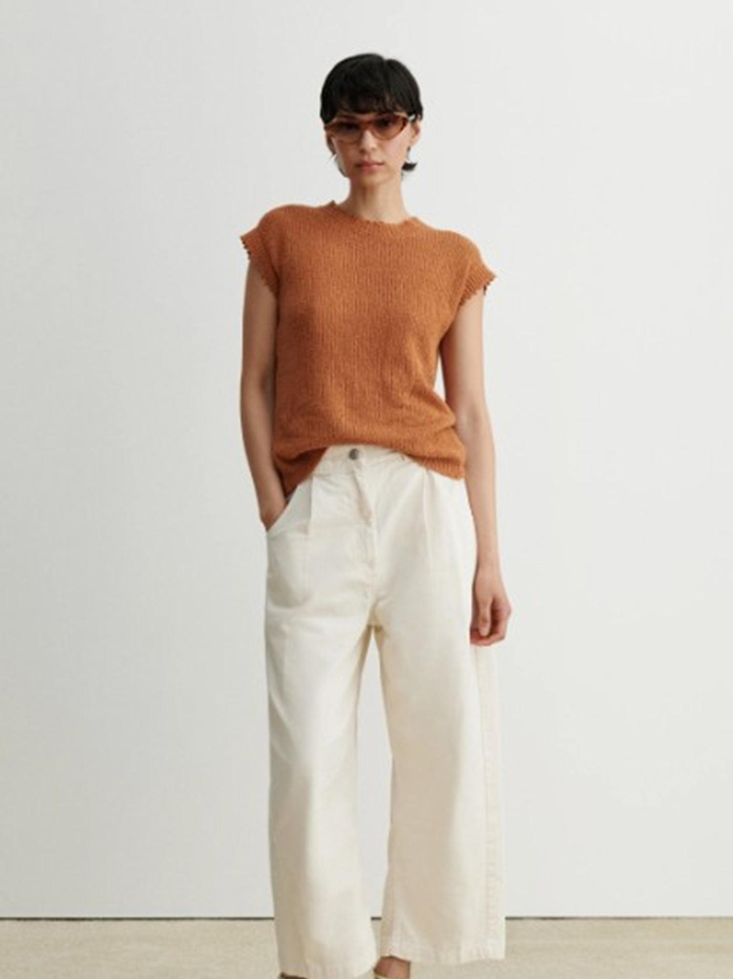 Person wearing a rust-colored top and white pants on a plain background