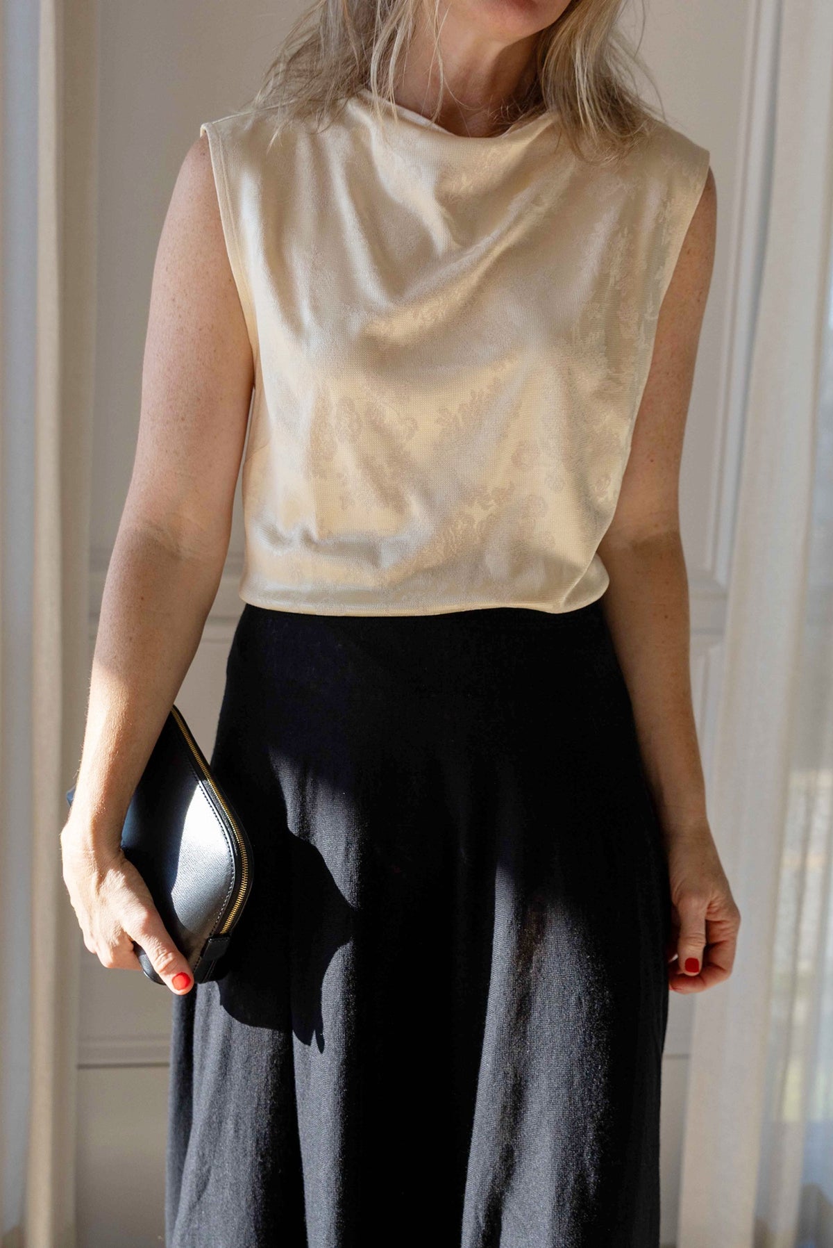 Close-up of the by Malene Birger Geri Skirt in black with a cream sleeveless top, holding a black leather cosmetics case