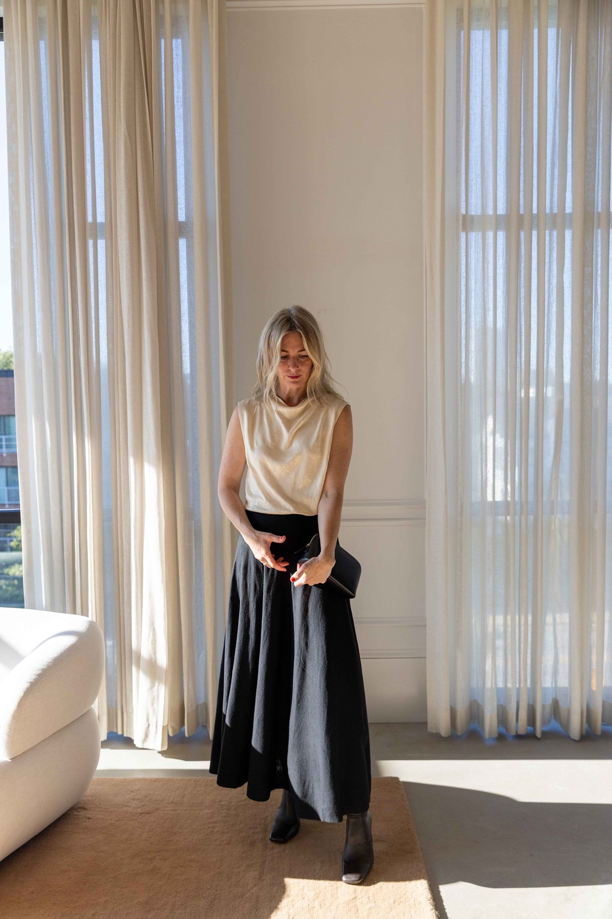 by Malene Birger Geri Skirt in black, A-line maxi skirt styled with a cream sleeveless top and black cosmetics case, full-length view