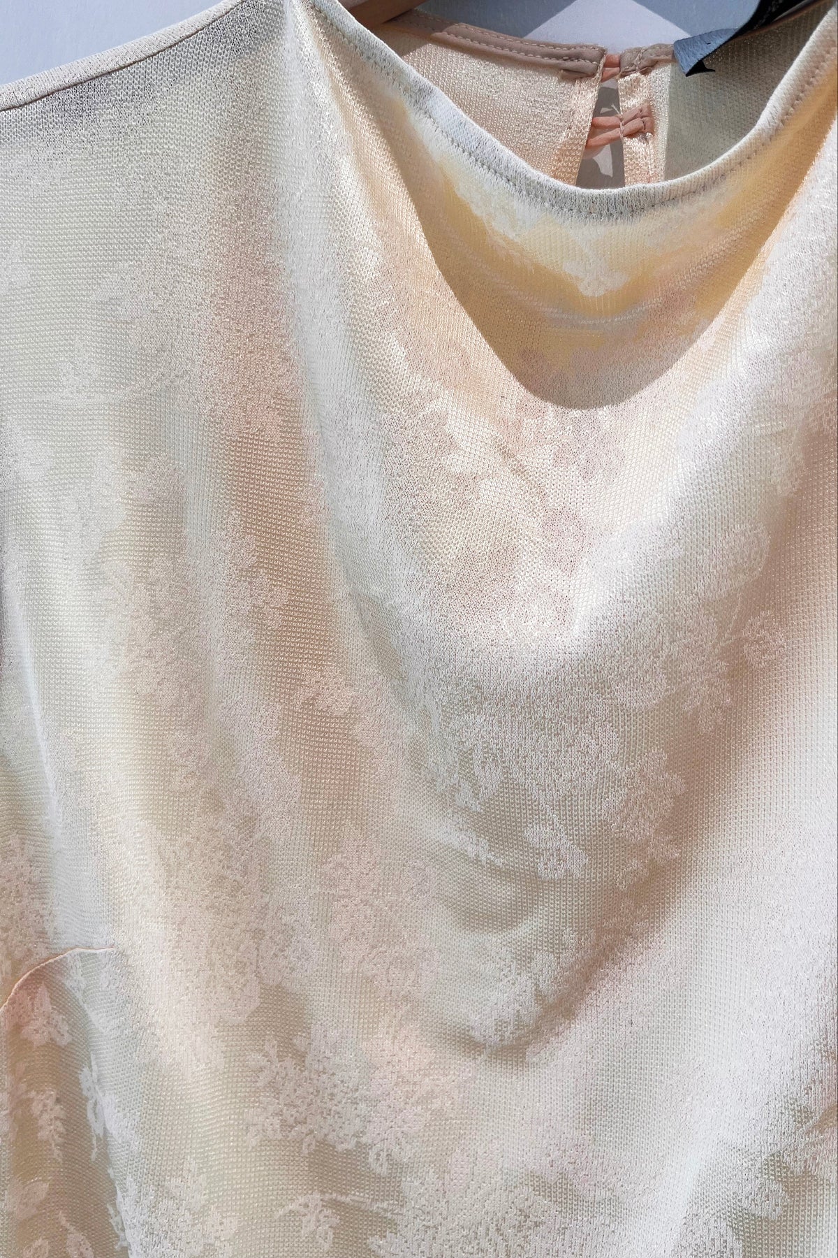 A close-up of a sleeveless cream-colored top with a subtle tonal floral jacquard pattern, featuring a scoop neckline and a visible lace-up back closure.