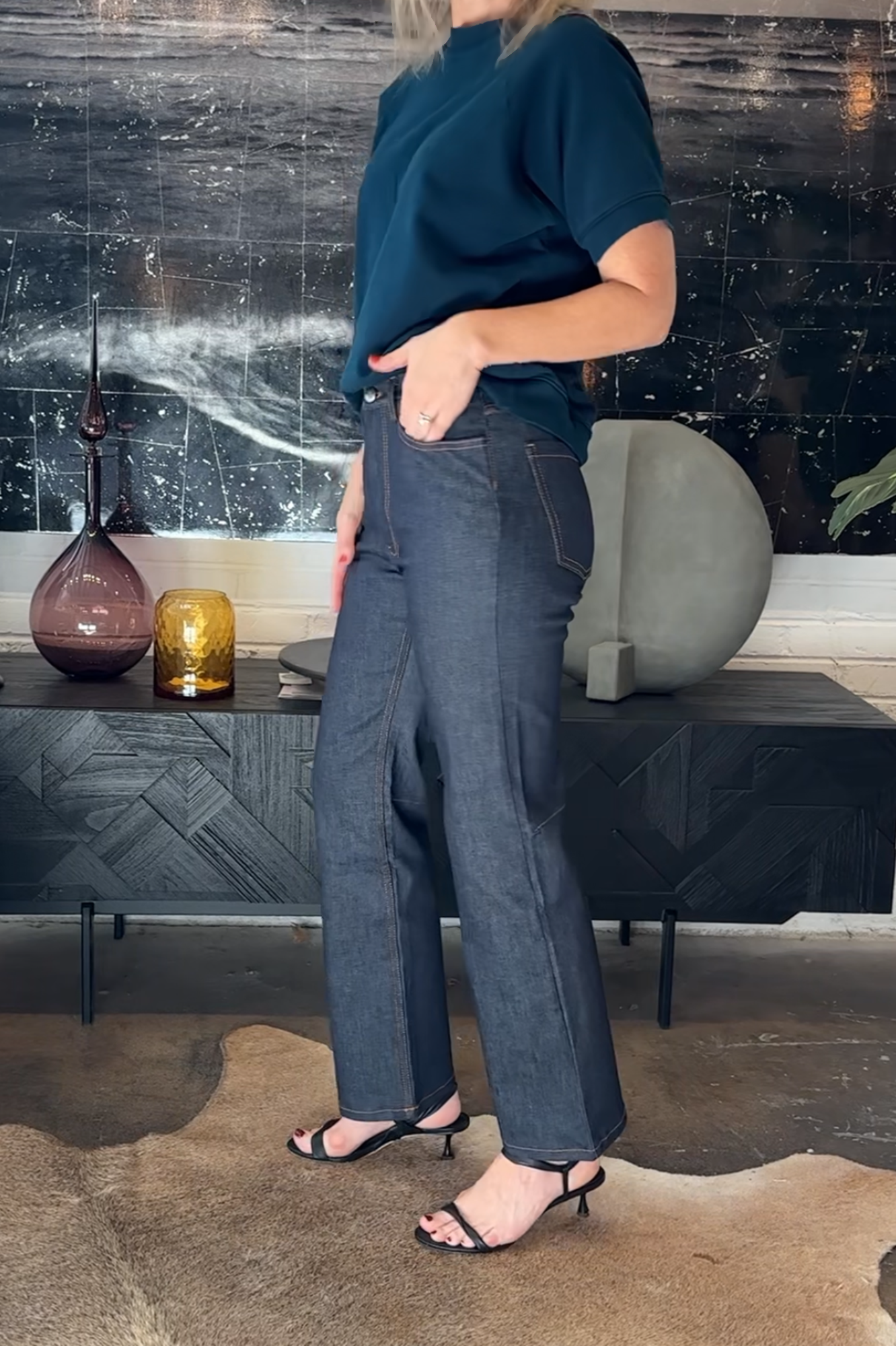 Person wearing a blue top and dark jeans standing in a room with decorative elements.