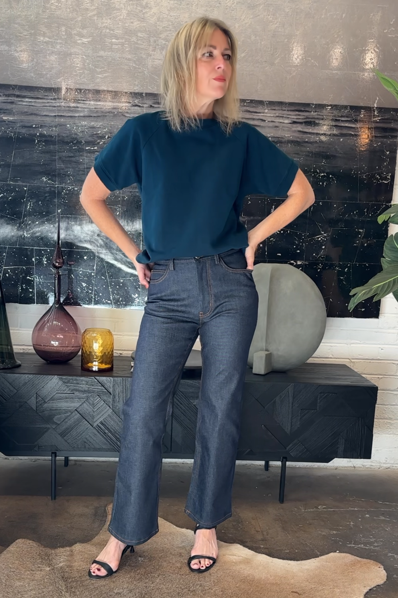 Woman in a blue top and jeans standing in a modern living room.