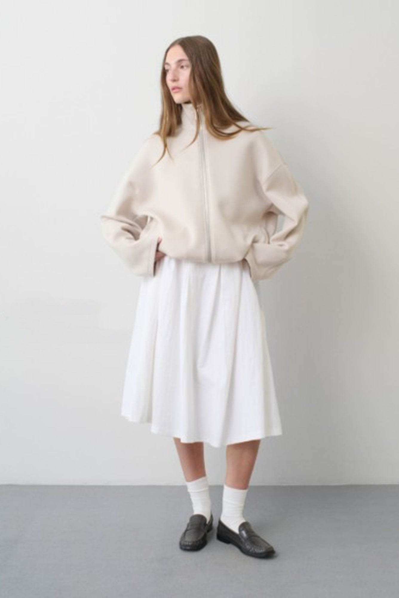 Woman wearing a beige jacket over a white dress on a plain background