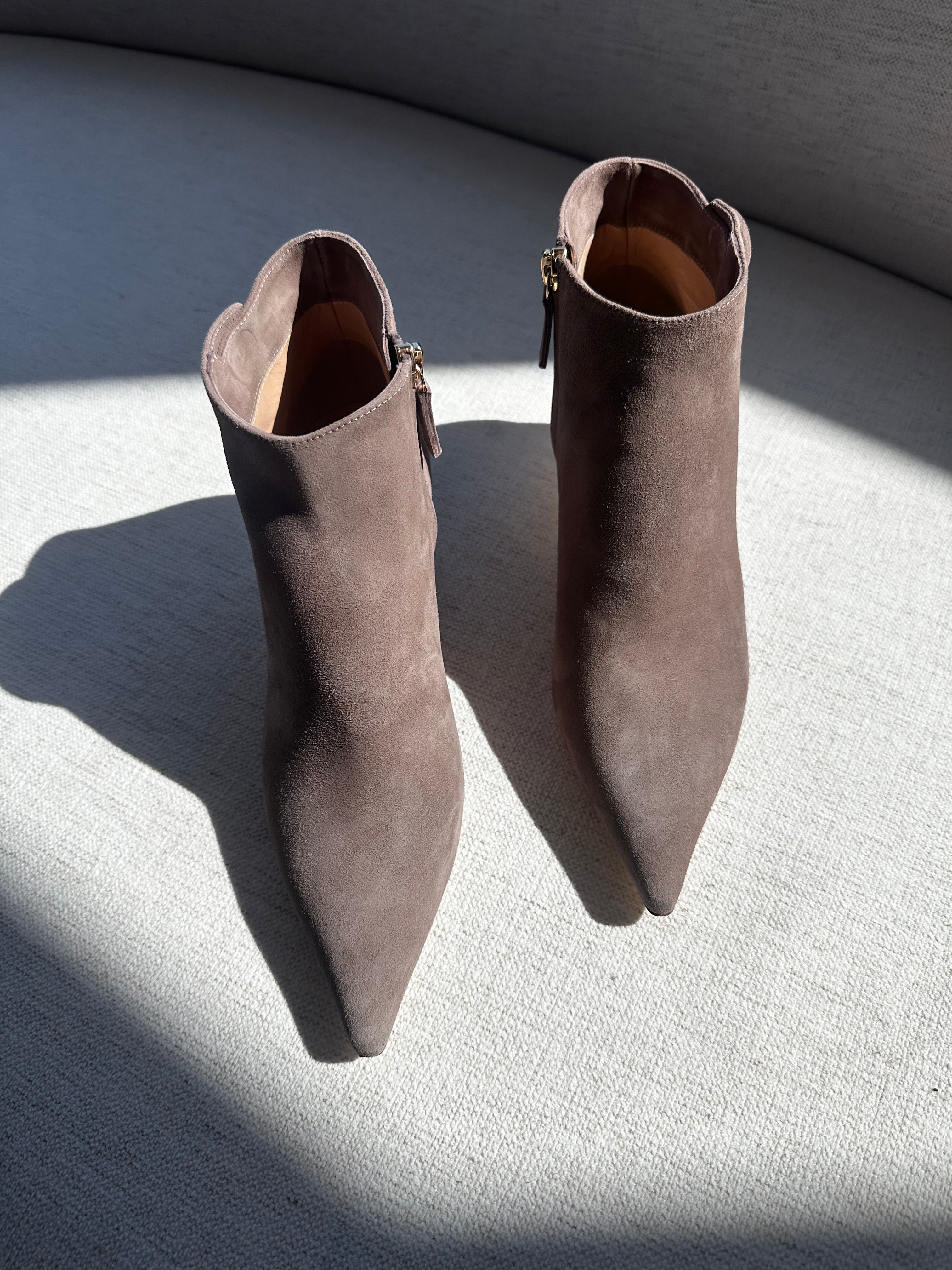Pair of brown suede ankle boots on a textured surface with a light source casting shadows.