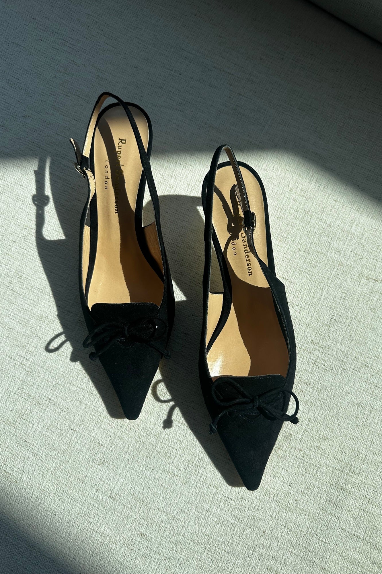 Black high-heeled shoes with bow details on a textured surface