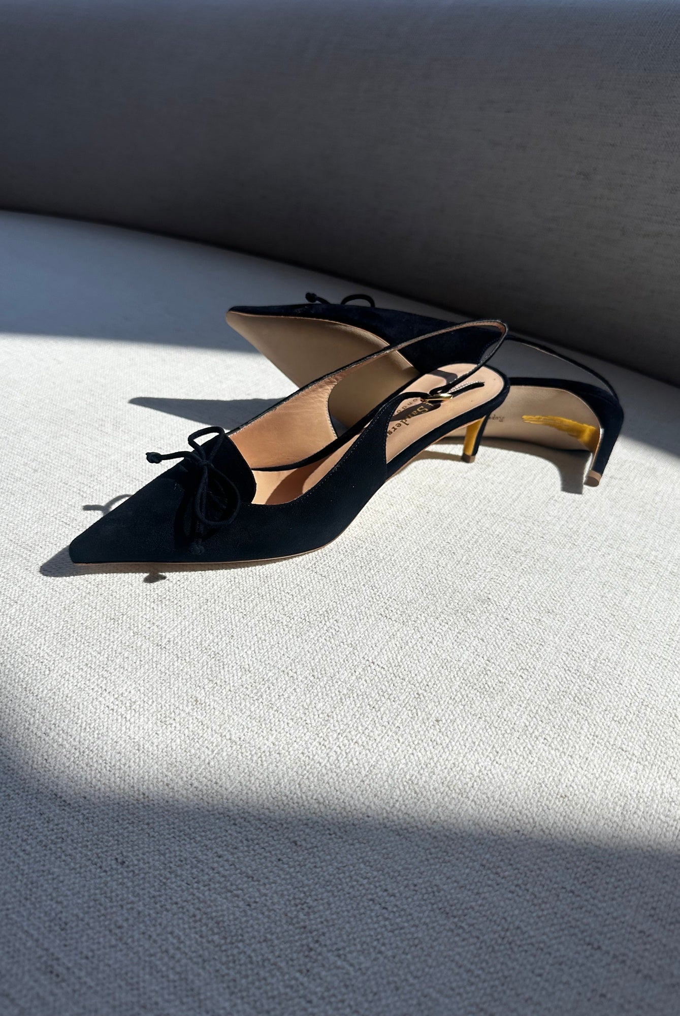 Black high-heeled shoes with bow details on a light gray surface.