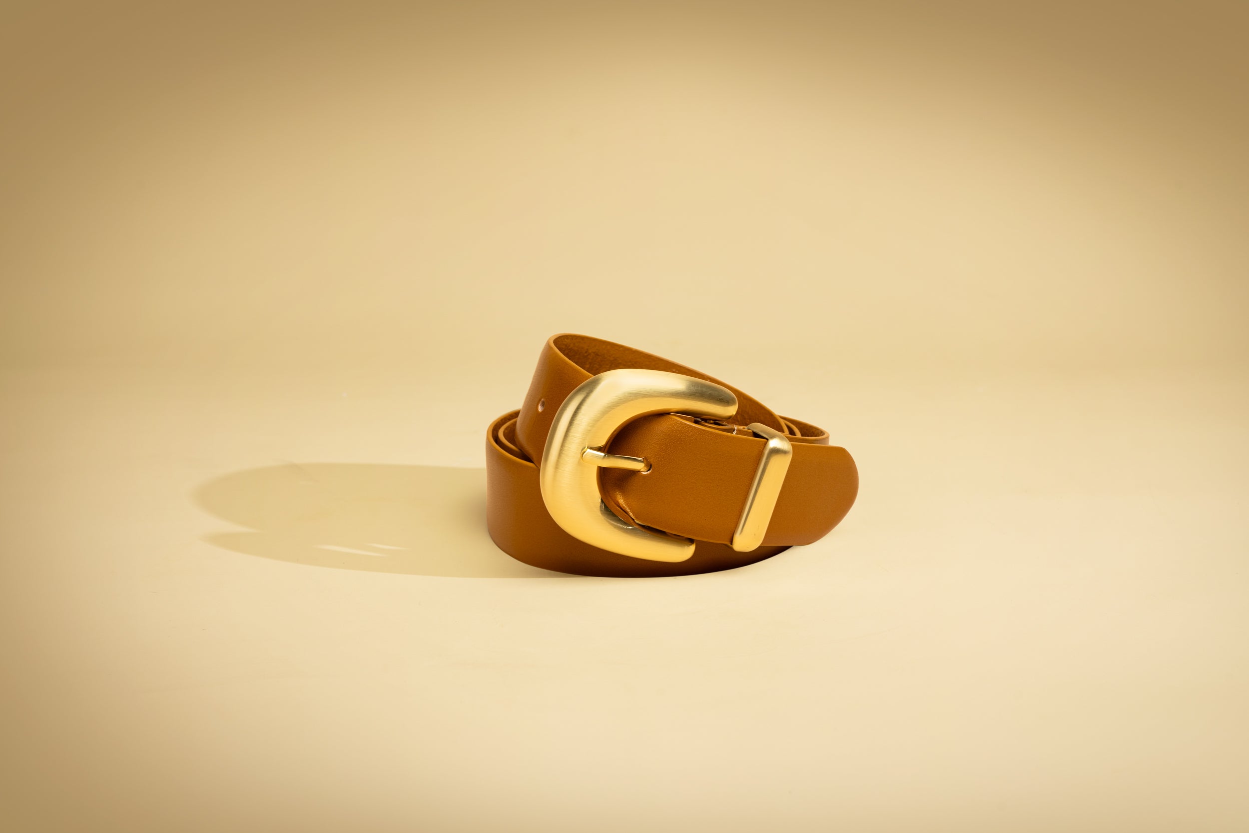 Brown leather belt with gold buckle on a beige background